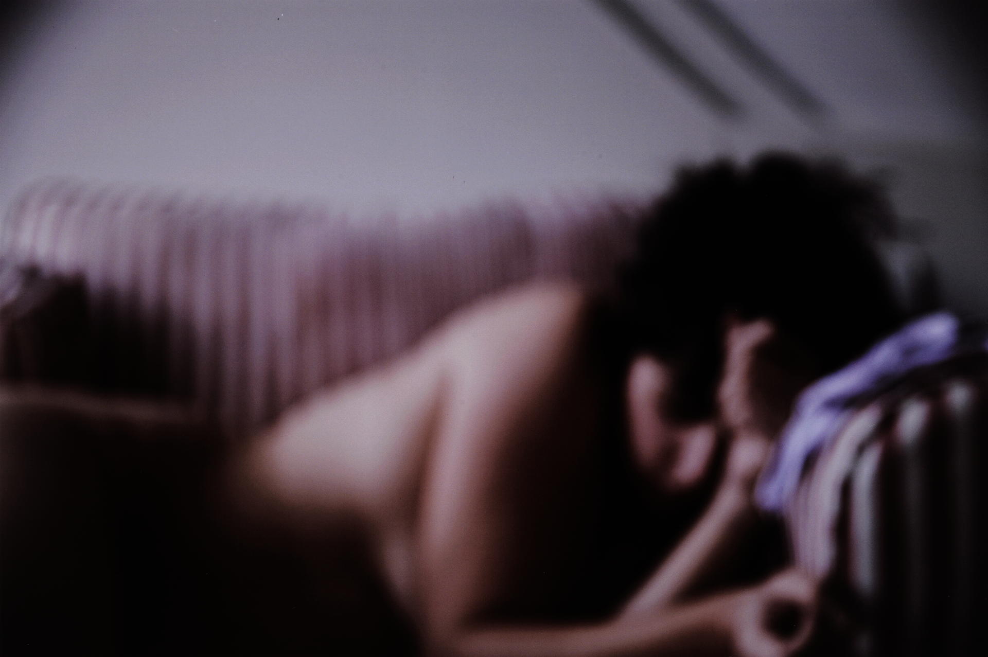 Blurry photo of a light-skinned woman from the waist up. She leans on her elbows and gazes down.
