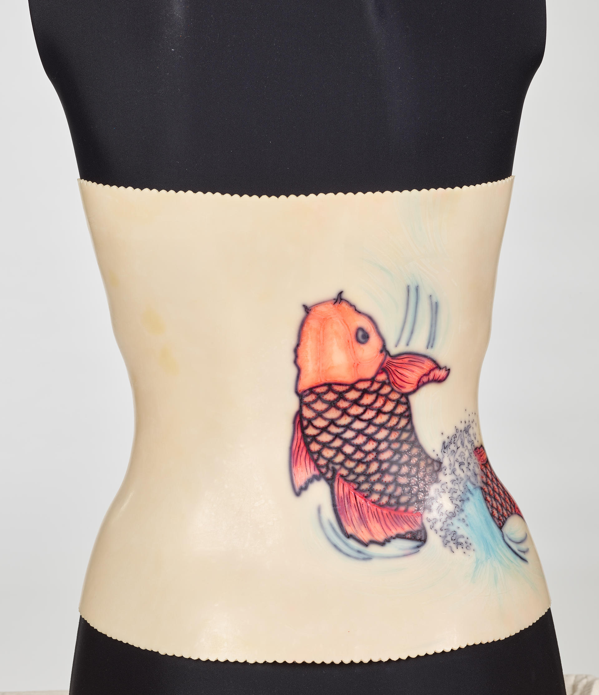 An off-white back brace is molded onto a black mannequin torso. The plastic brace attaches down the middle of the torso. A red koi design decorates the right side.