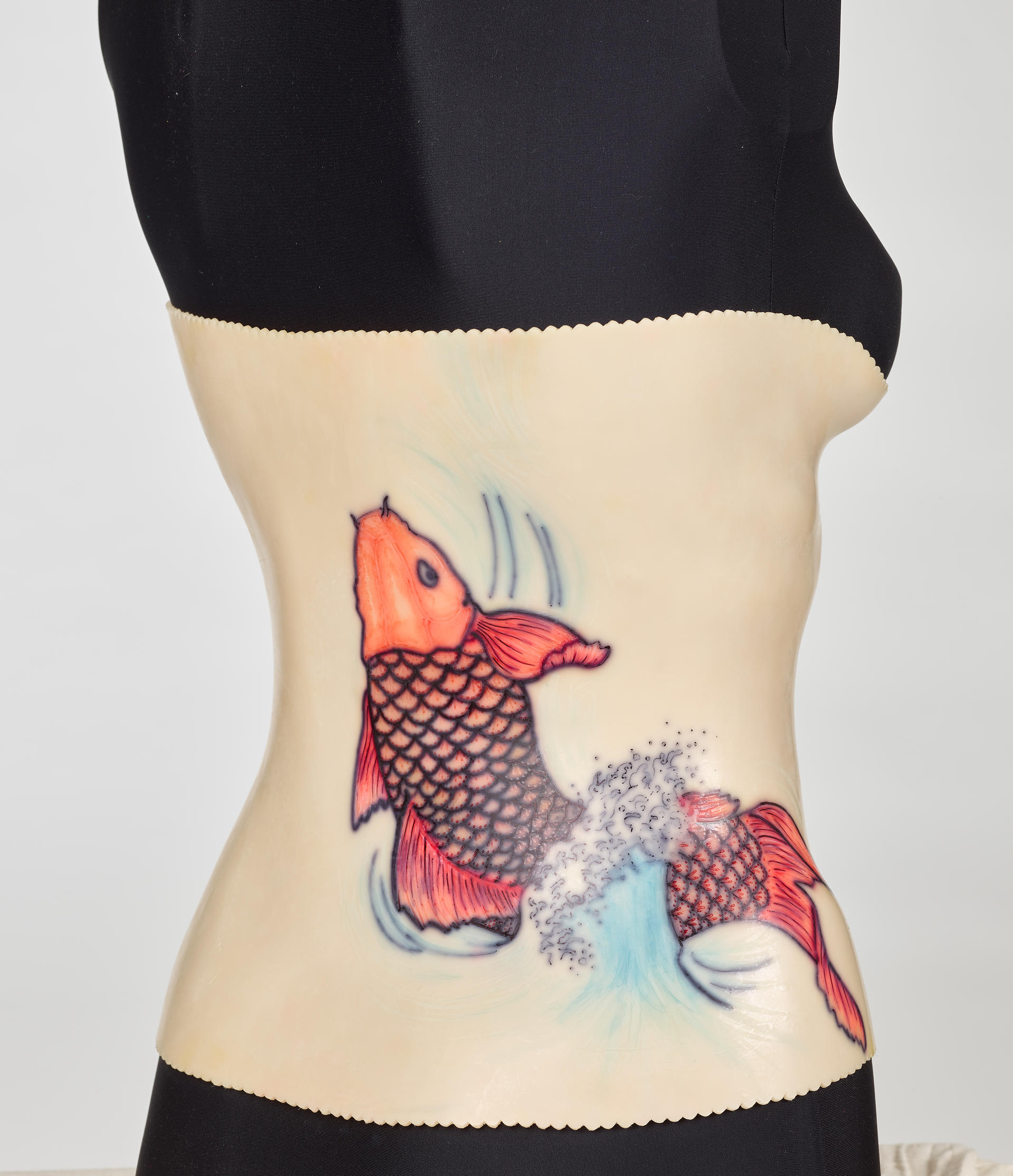 An off-white back brace is molded onto a black mannequin torso. The plastic brace attaches down the middle of the torso. A red koi design decorates the right side.