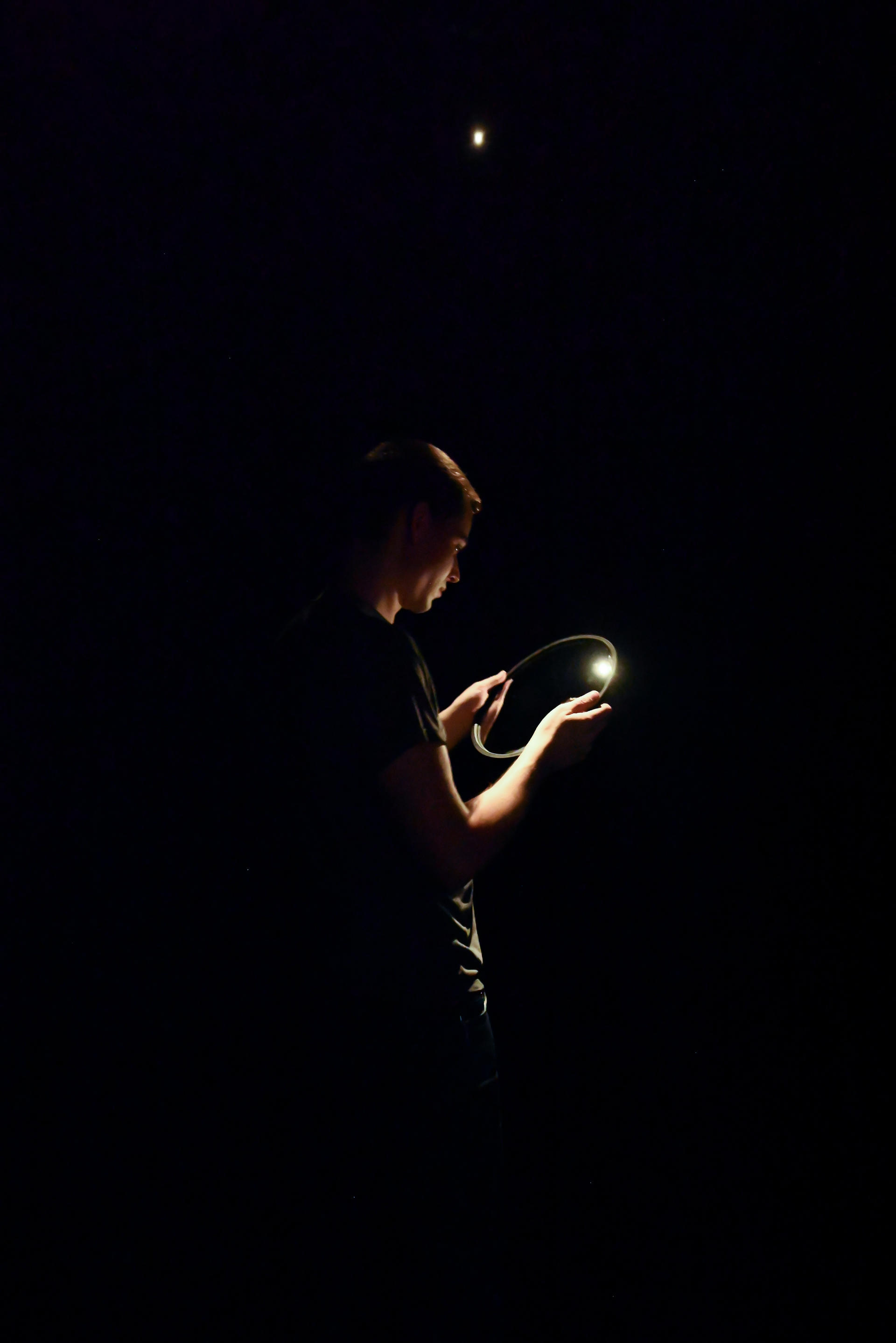 A dark void with the artist standing in the center illuminated. 