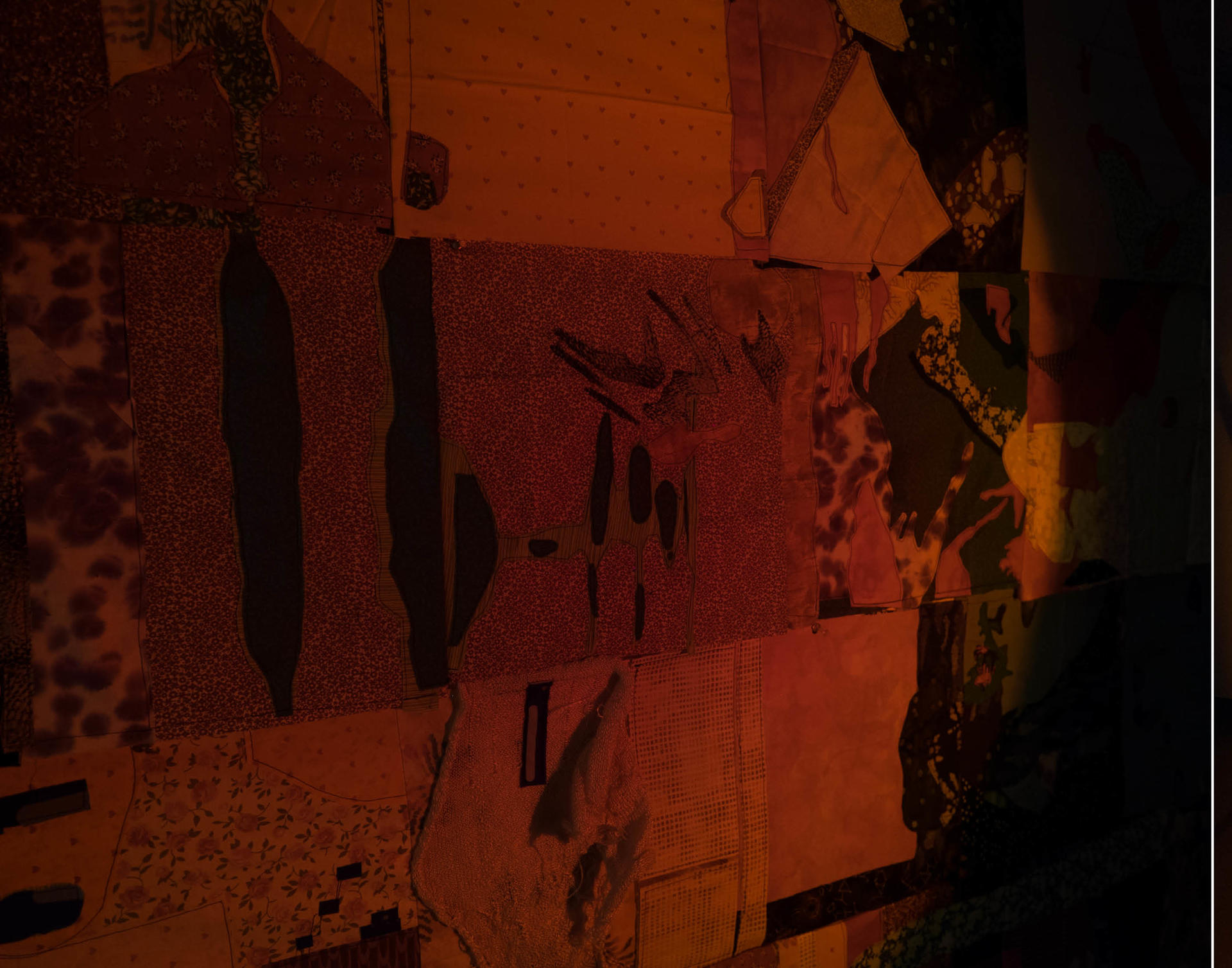 A quilt is pinned to a wall, many different patterns and colors form strange organic and geometric forms. A circle of warm light floods the quilt, it feels like a quiet, early morning in the mountains. On the edge of that circle, the quilt quickly dissolves into darkness.