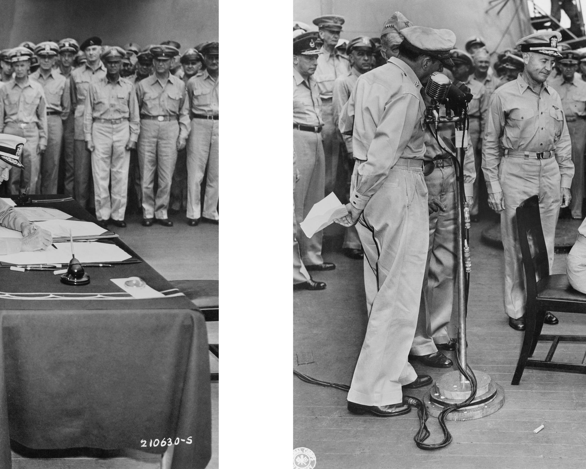 A black-and-white photograph of a crowd of soldiers looking on as a figure–cropped out of the frame–signs the document that officiates Japan's surrender at the close of World War II.