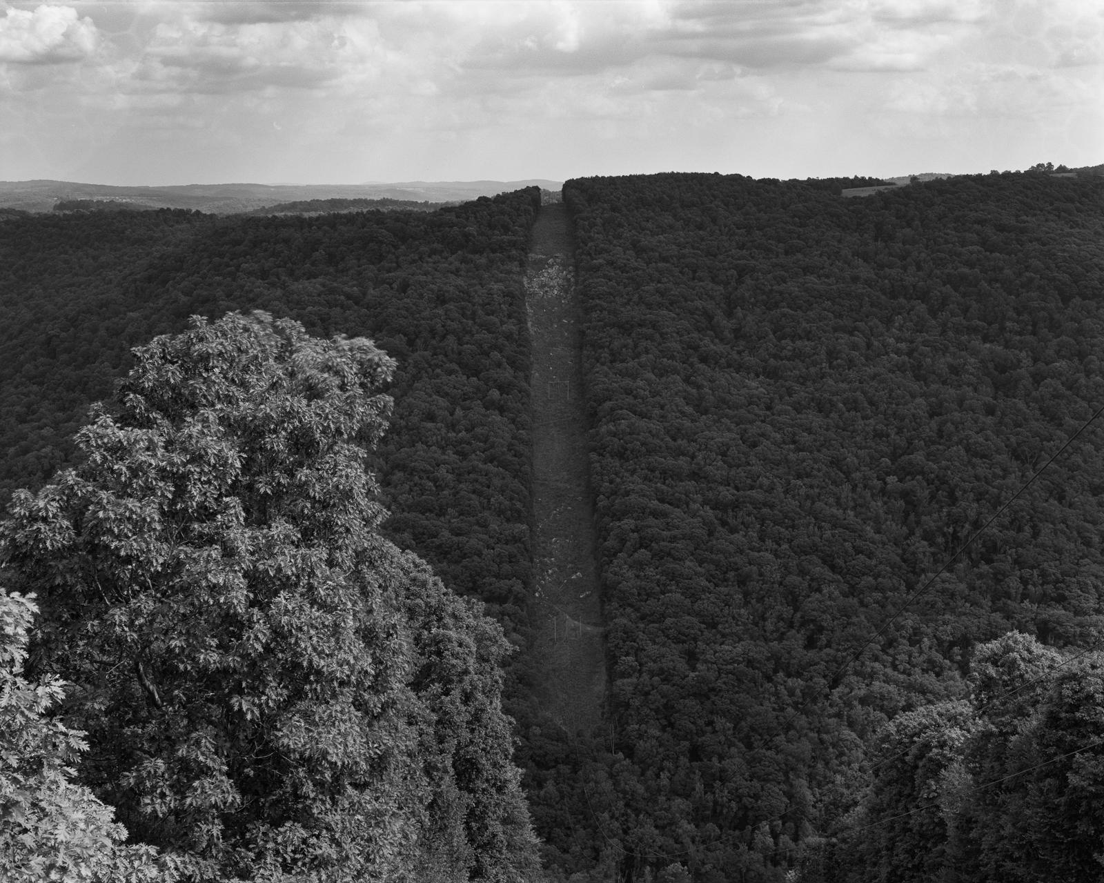 A landscape from the top of a mountain looking down into a valley. Down the middle of the image runs a cleared corridor for power lines.