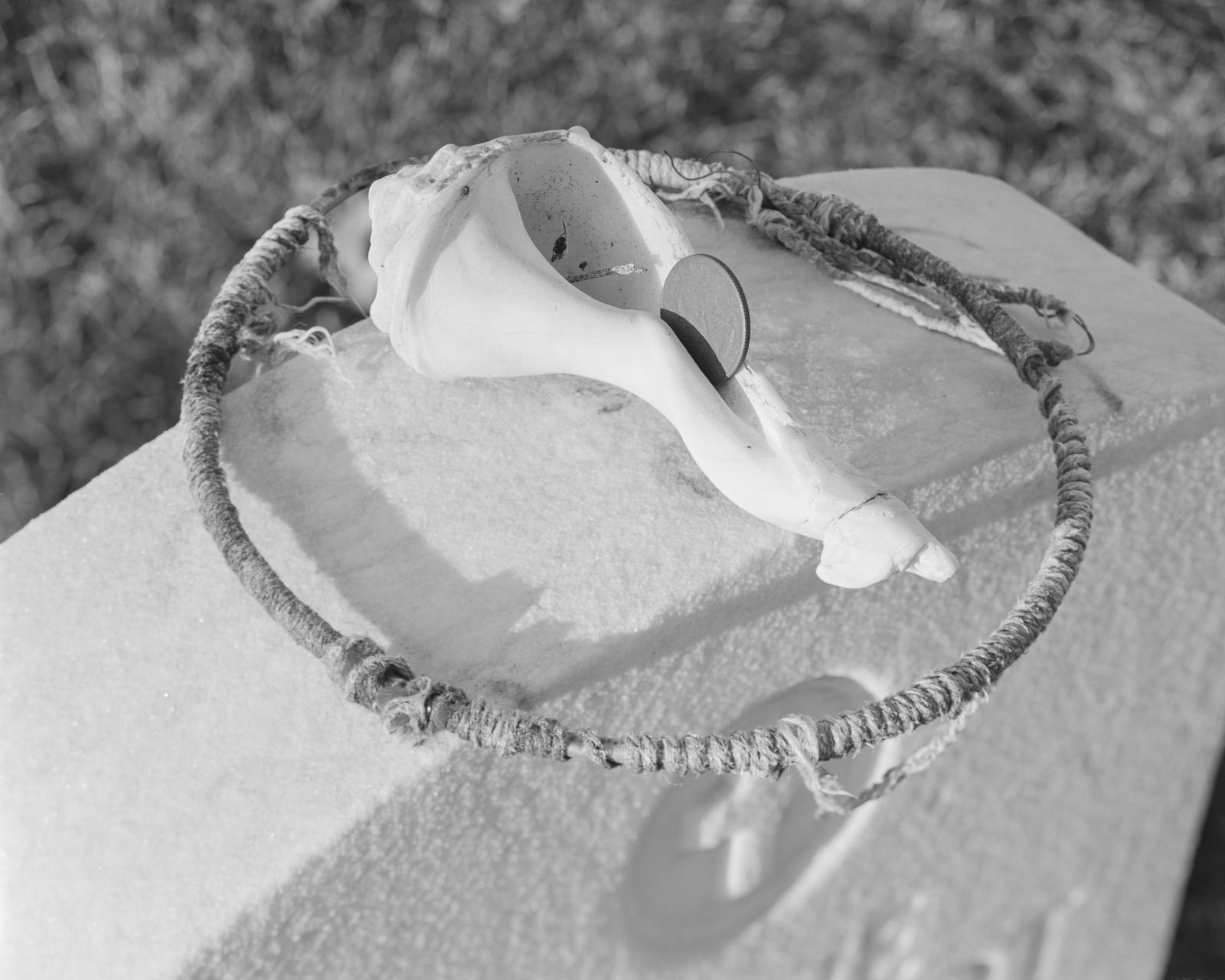 A gravestone is topped with a wooden hoop and a conch shell.