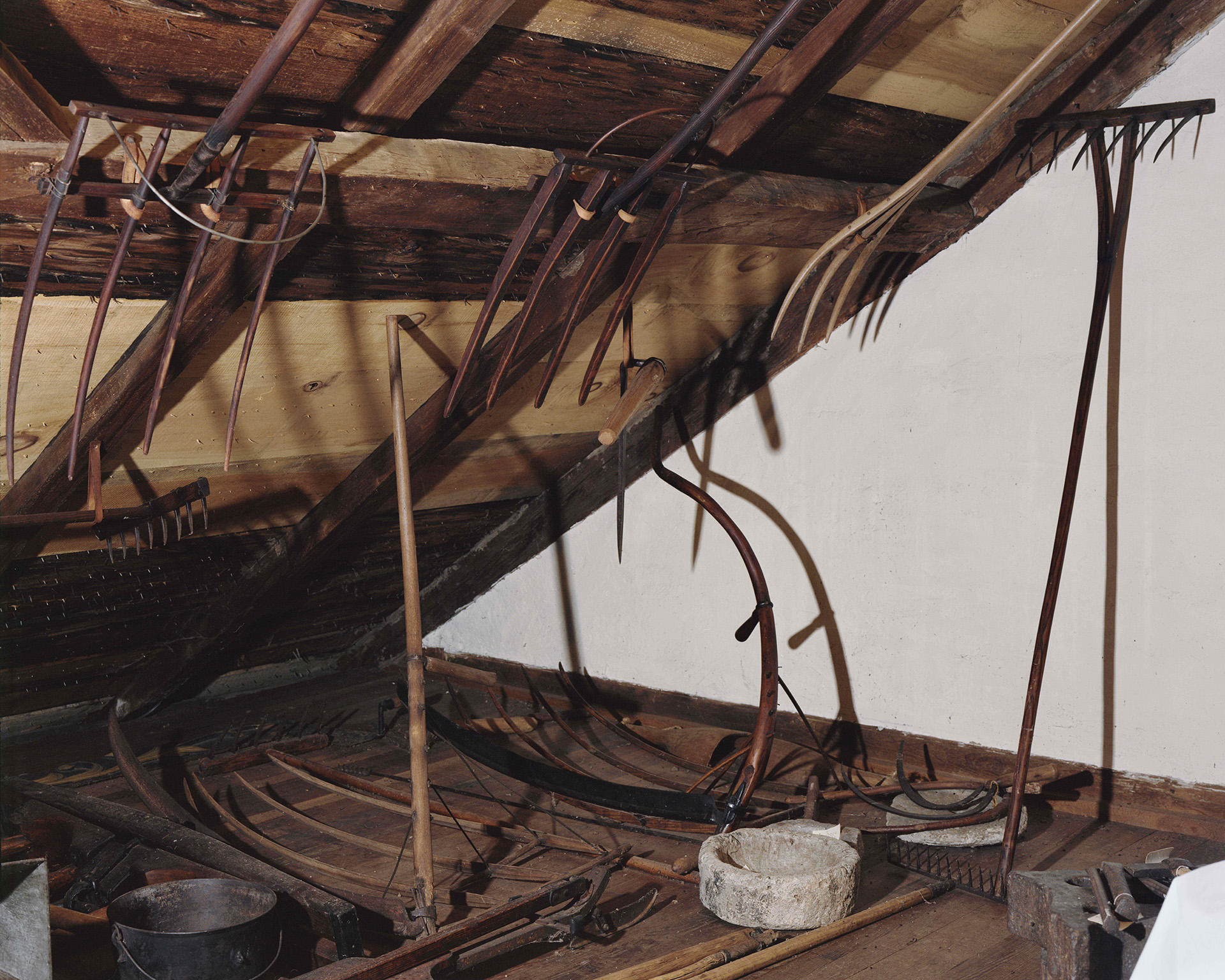Photograph of various farmings tools hung in a dark attic.