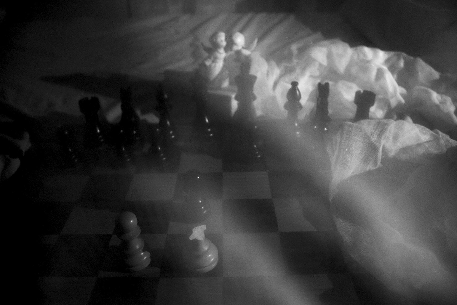 Chess board sitting on top of bed sheets a long with two porcelain angels in the background. 