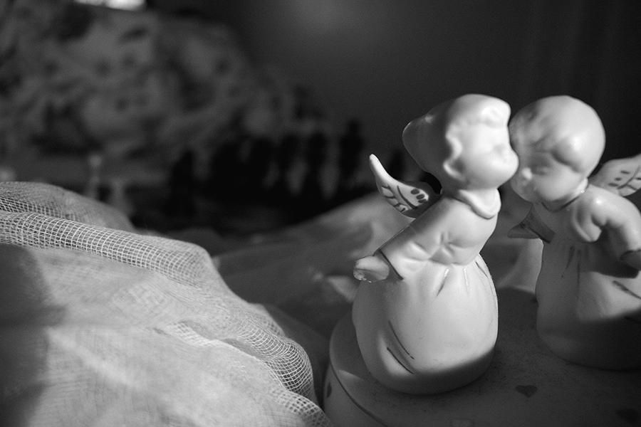 Chess board sitting on top of bed sheets a long with two porcelain angels in the foreground.