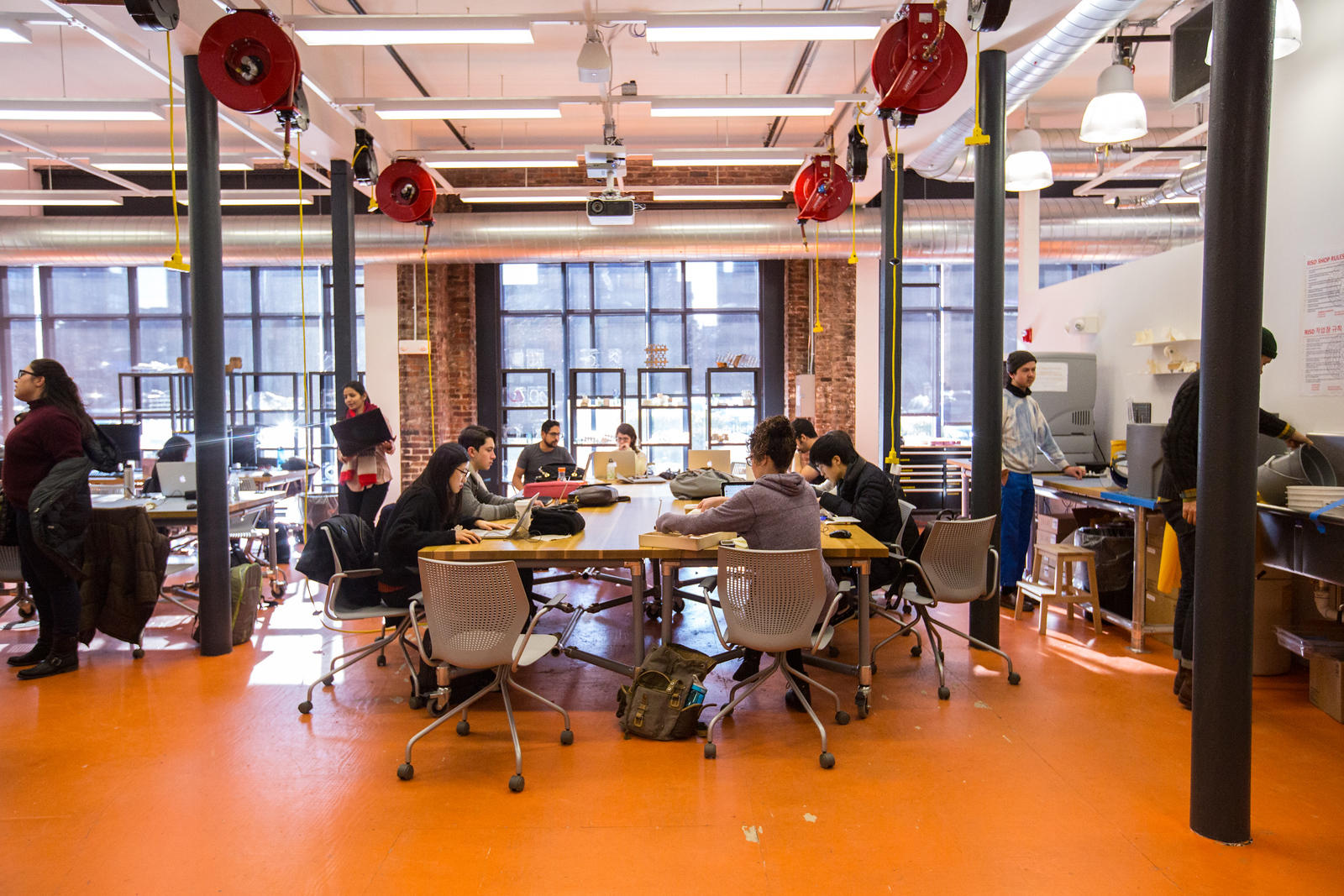 interior shot of co-works, showing students working at large tables in front of floor to ceiling windows. Laser cut and 3D printed objects sit on shelves behind.