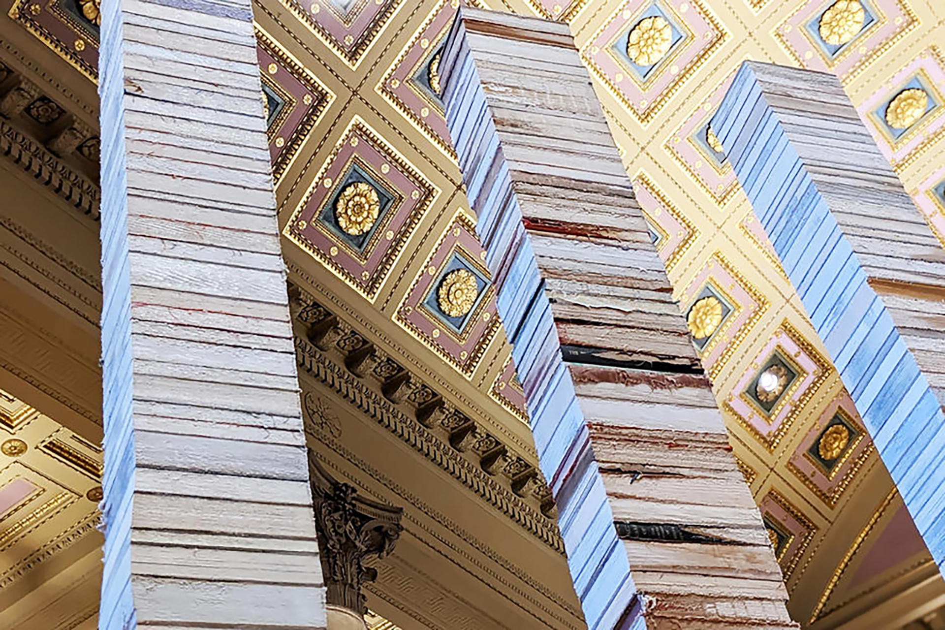 Three towering columns of stacked books reach towards an ornate golden ceiling.