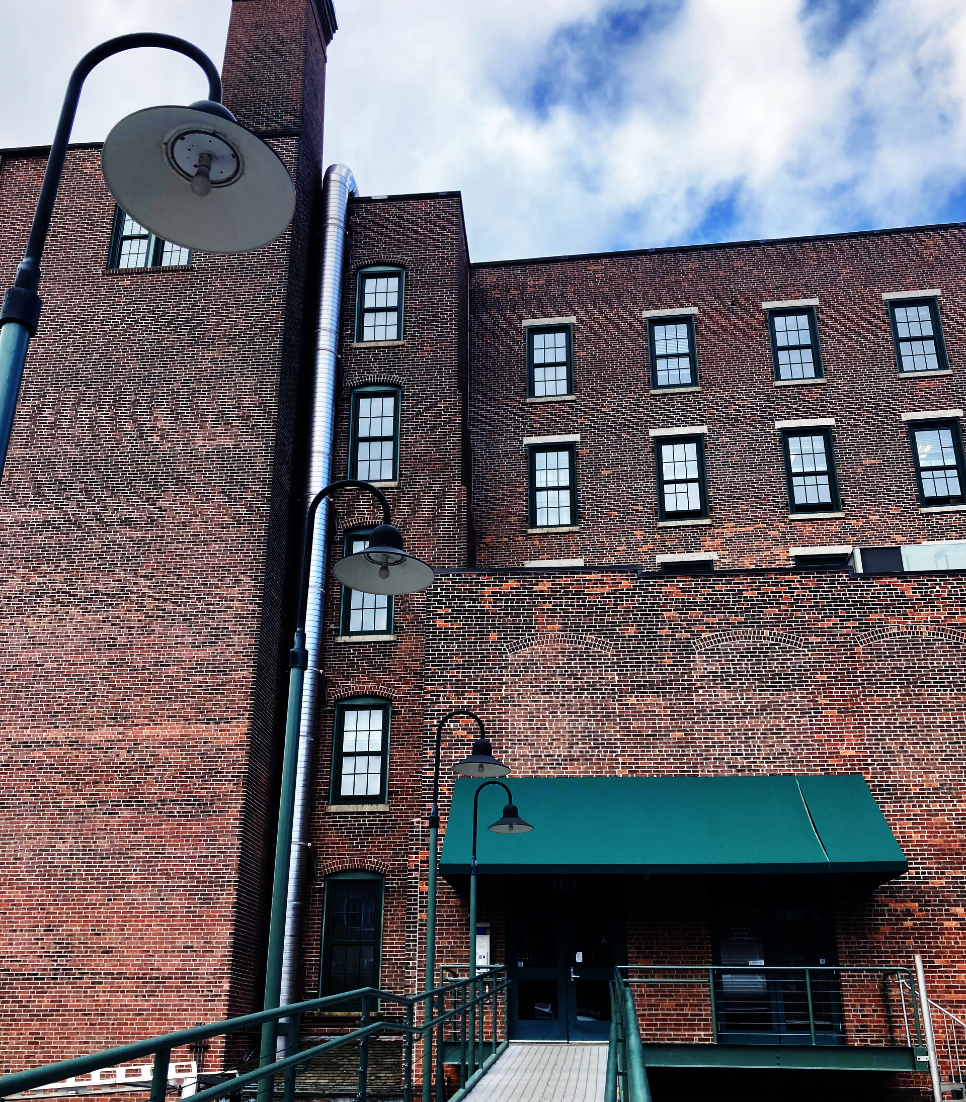 5 story brick building, viewed from the front as if walking up the ramp to its entrance. The entrance has a green awning.