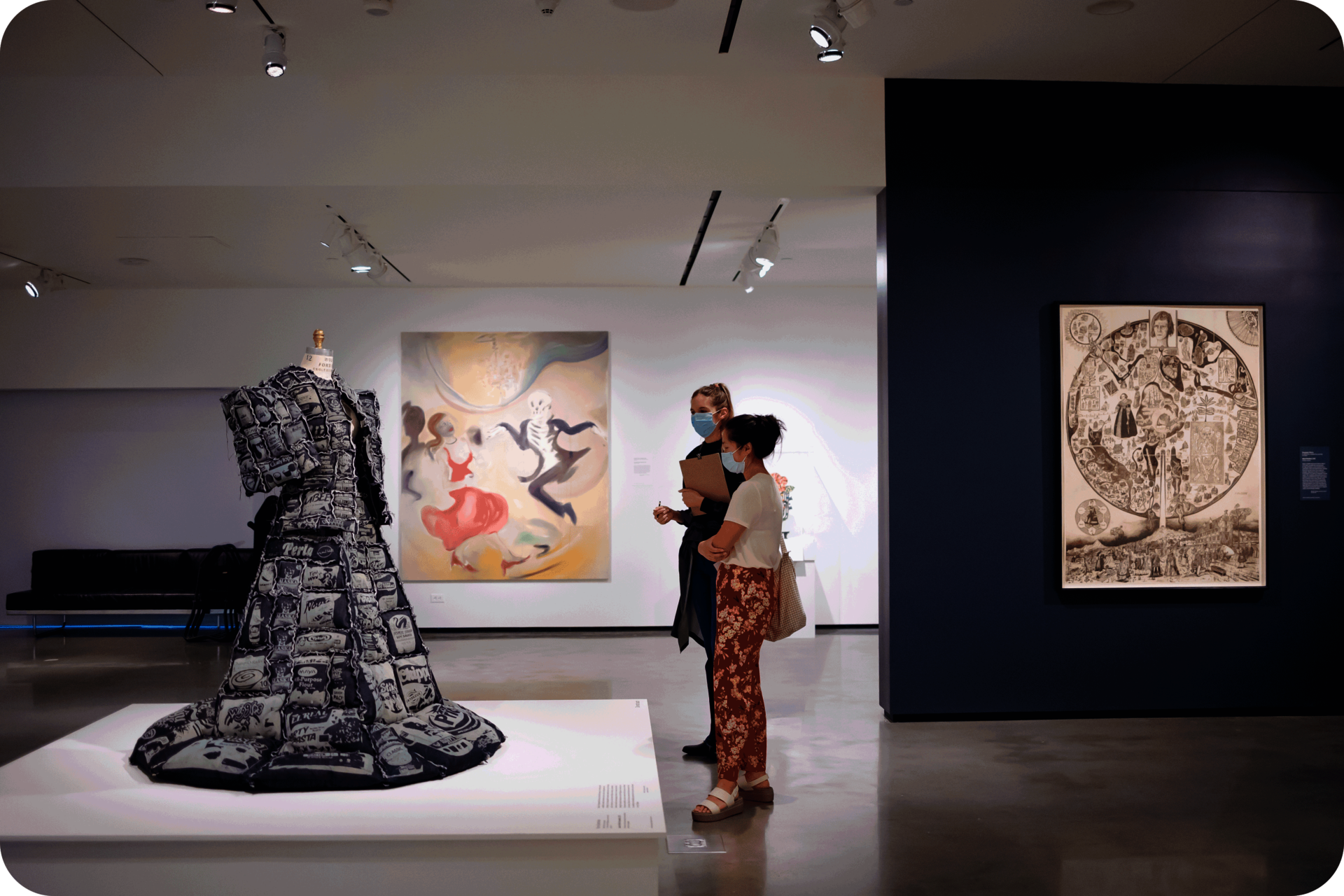 Two people looking at a mannequin wearing a bulky dress. Besides them is a blue wall featuring a monochromatic work, and behind them is a large oil painting. 