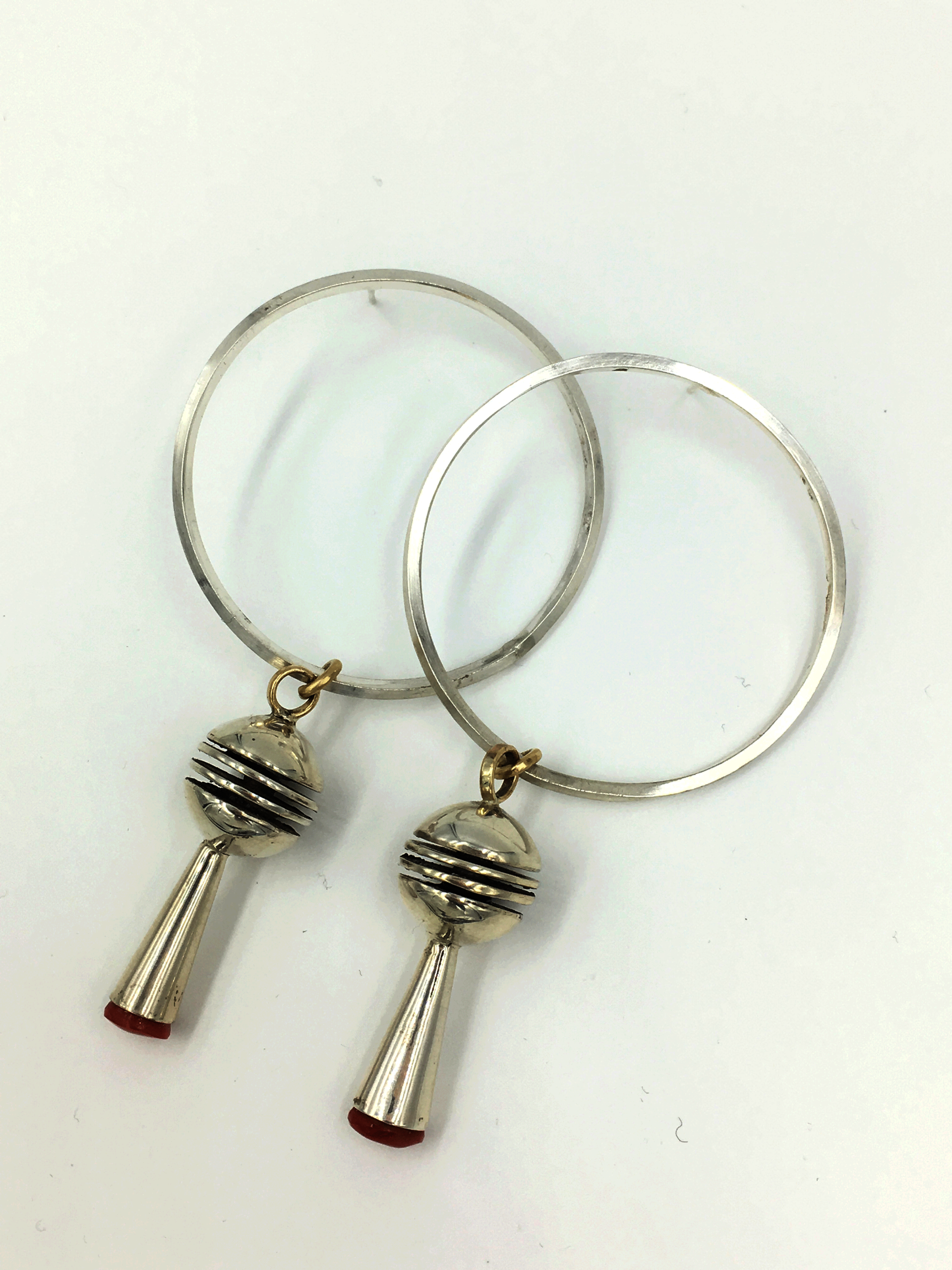 A pair of silver hoop earrings against a white background, laid out so that the hoops overlap. Their bases both feature attached silver spheres with a long silver cone. 