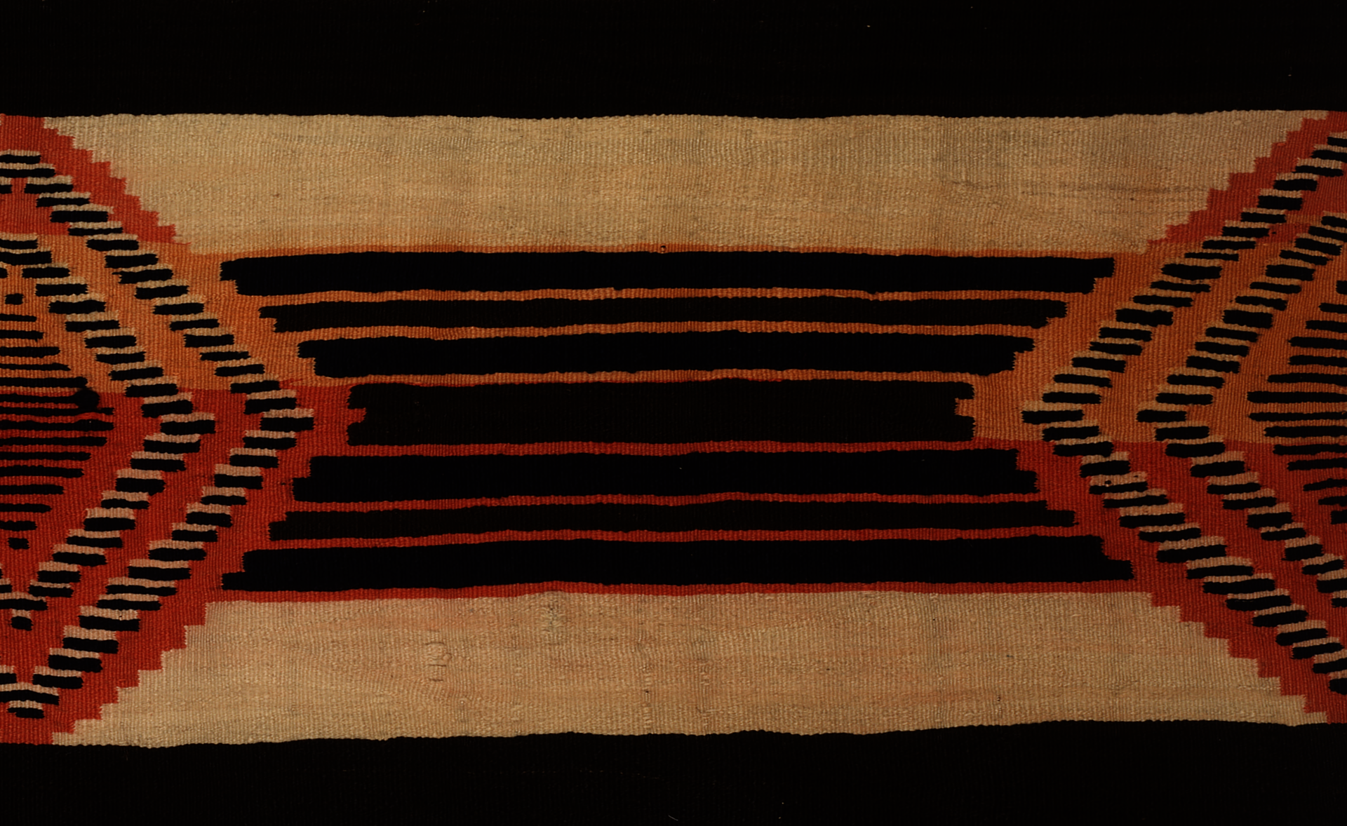 A woven textile with black and orange stripes of various sizes and shapes on a tan colored background. 