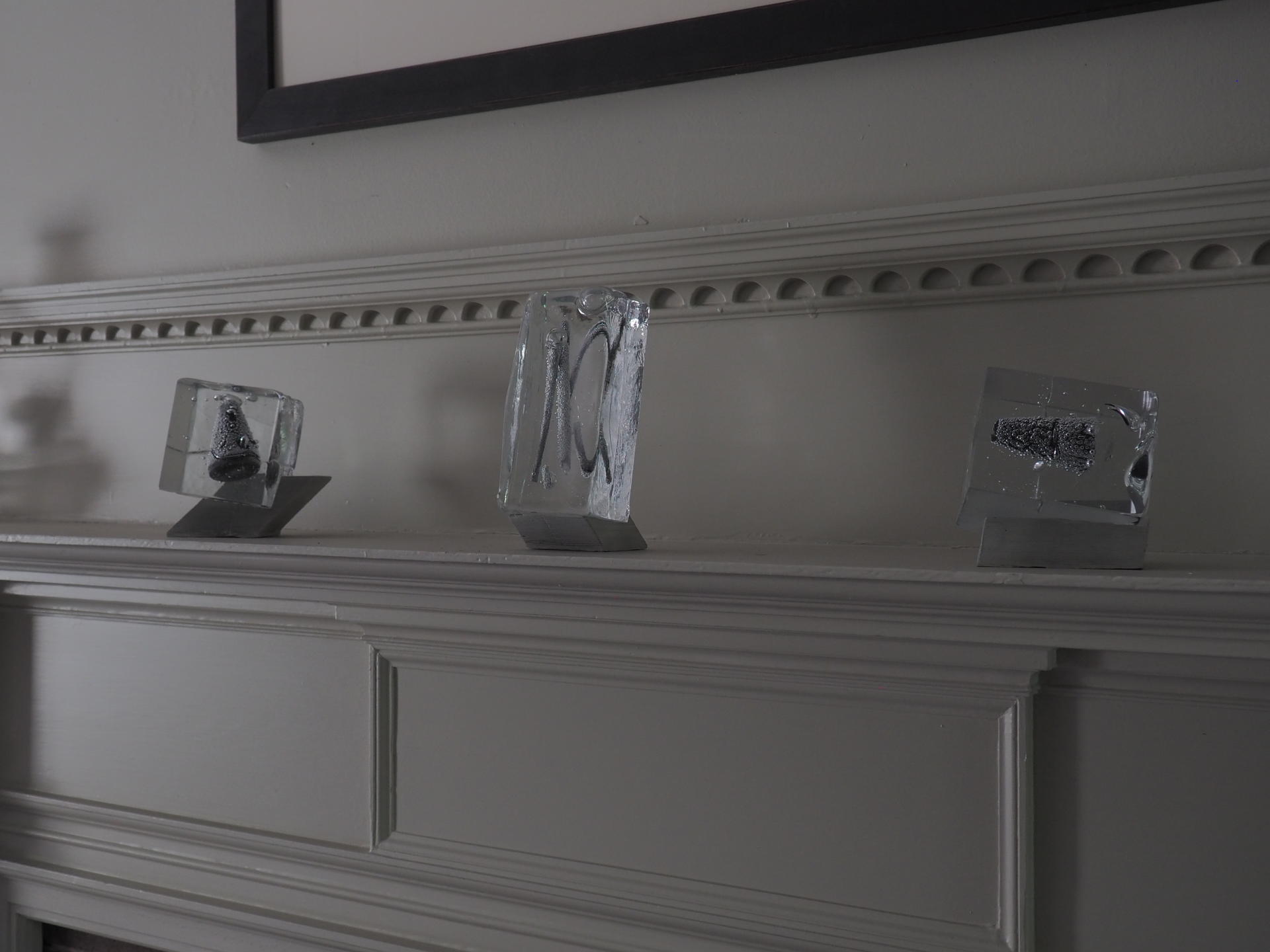 Three glass objects on concrete stands sitting on a fireplace mantle. 