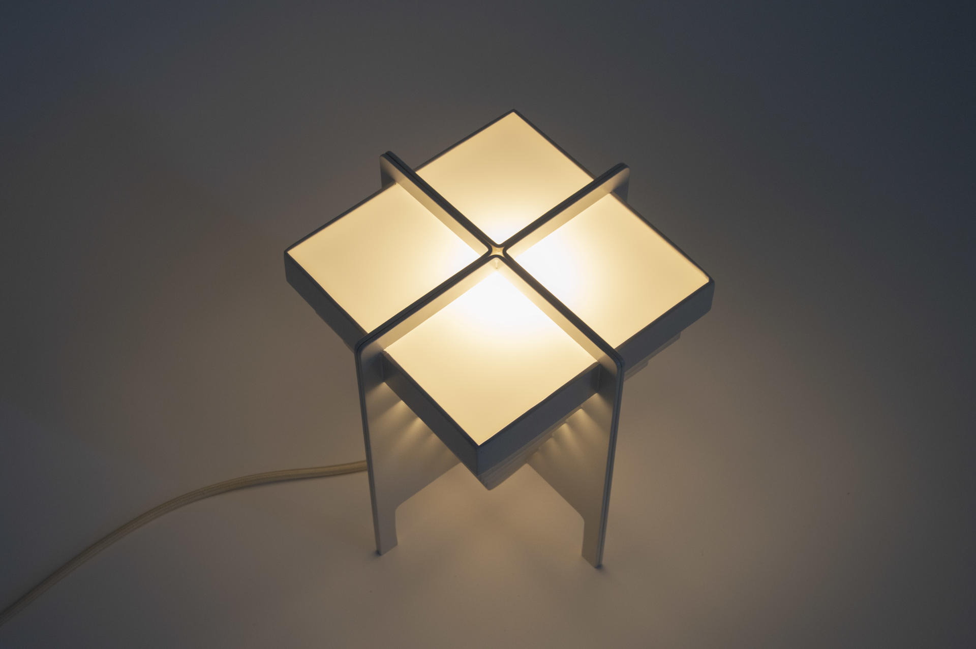 A lamp made of four repeated units and arranged in a way to emphasize the gap between the elements. 