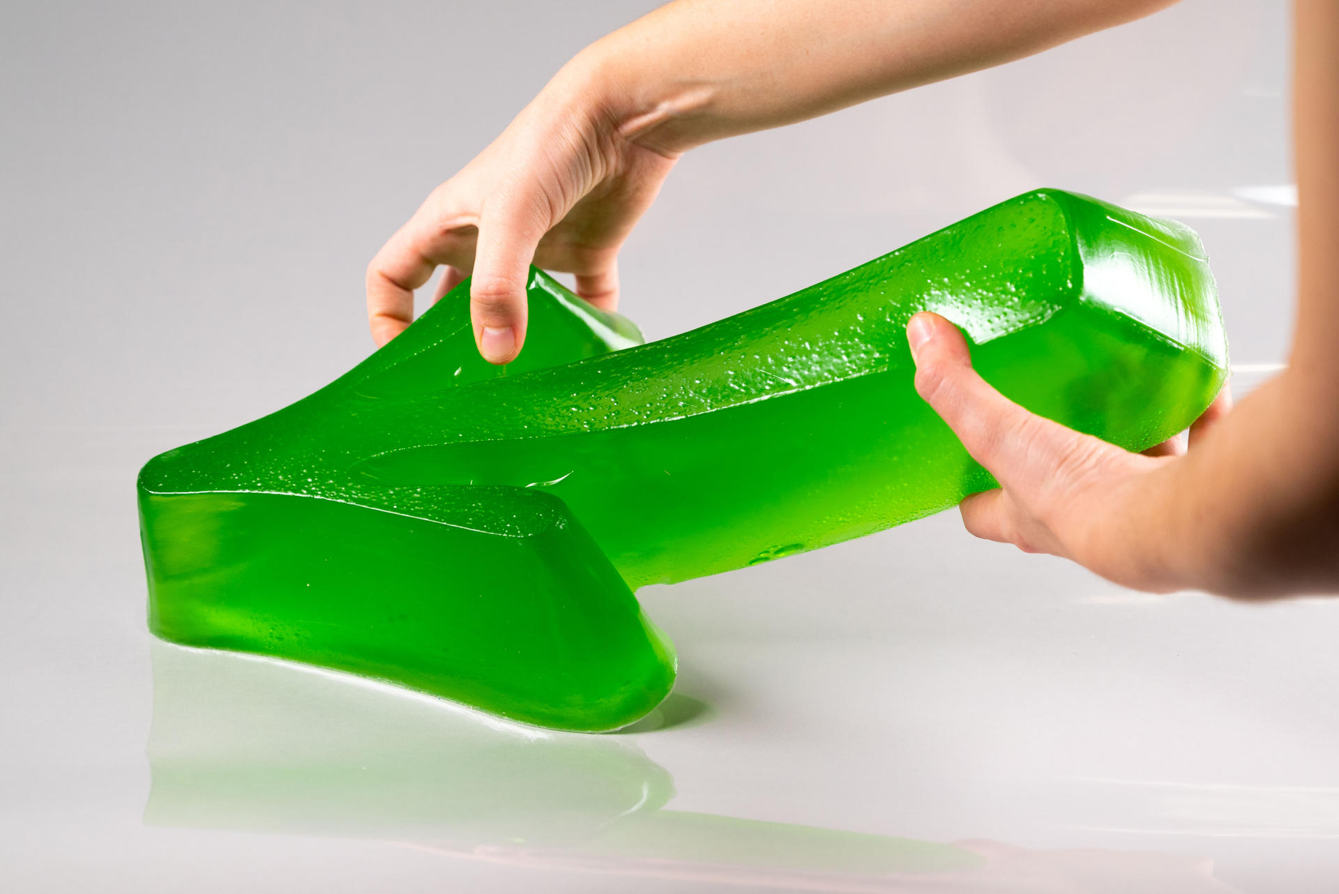 Green gelatin semi-transparent arrow-shaped sculpture, held by two hands.