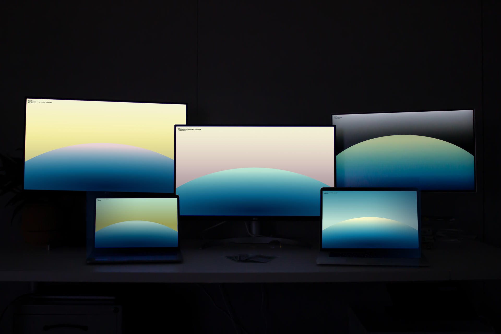 Five computer monitors of different sizes display a colorful screen saver design.