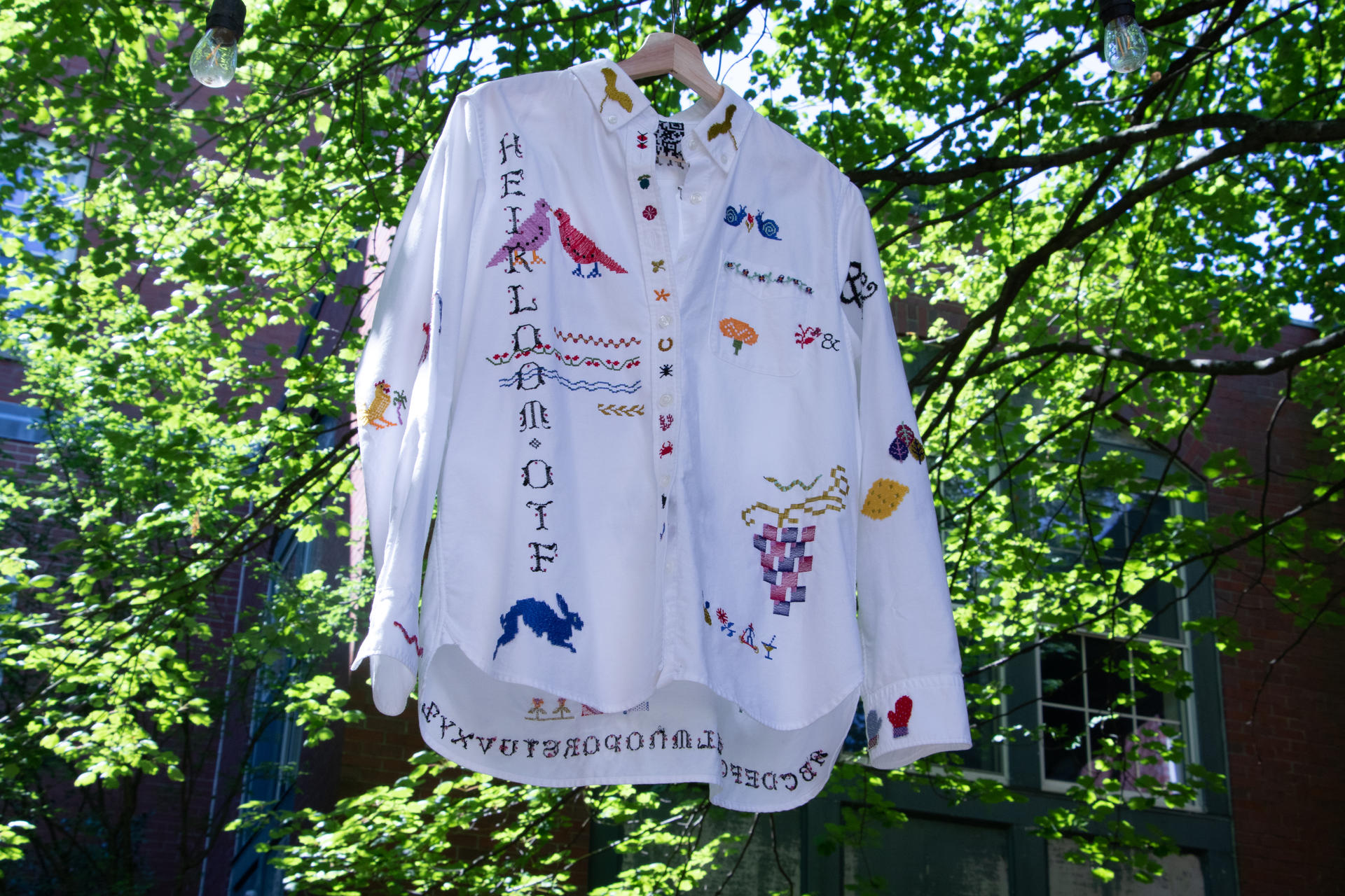 A hanging white-collared shirt that has been embroidered with colorful type and symbols.