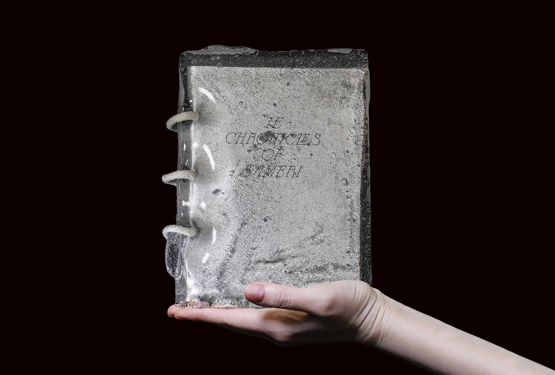 A hand holding a book with thick glass cover and rope binding.