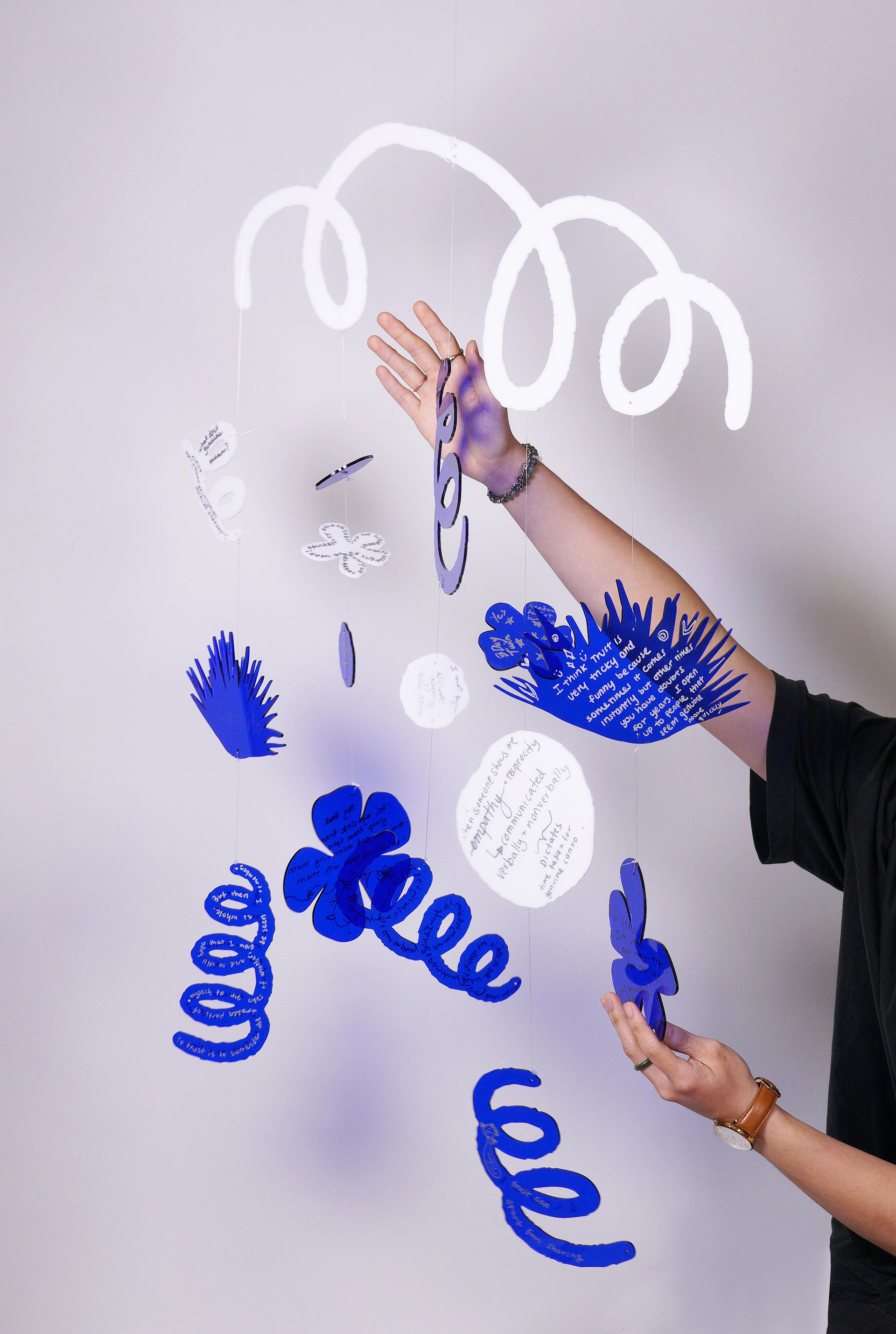 A mobile with transparent blue and white plexiglass cut in shapes of flowers and plants.