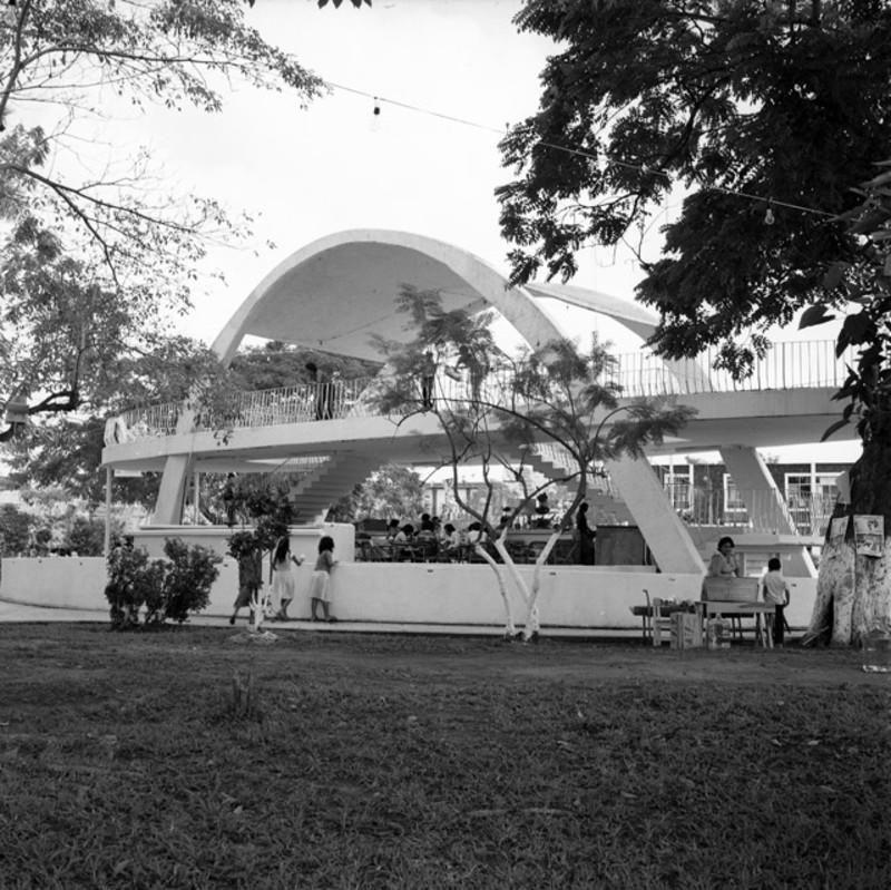 A group of children play underneath an arched, Modernist pavillion. 