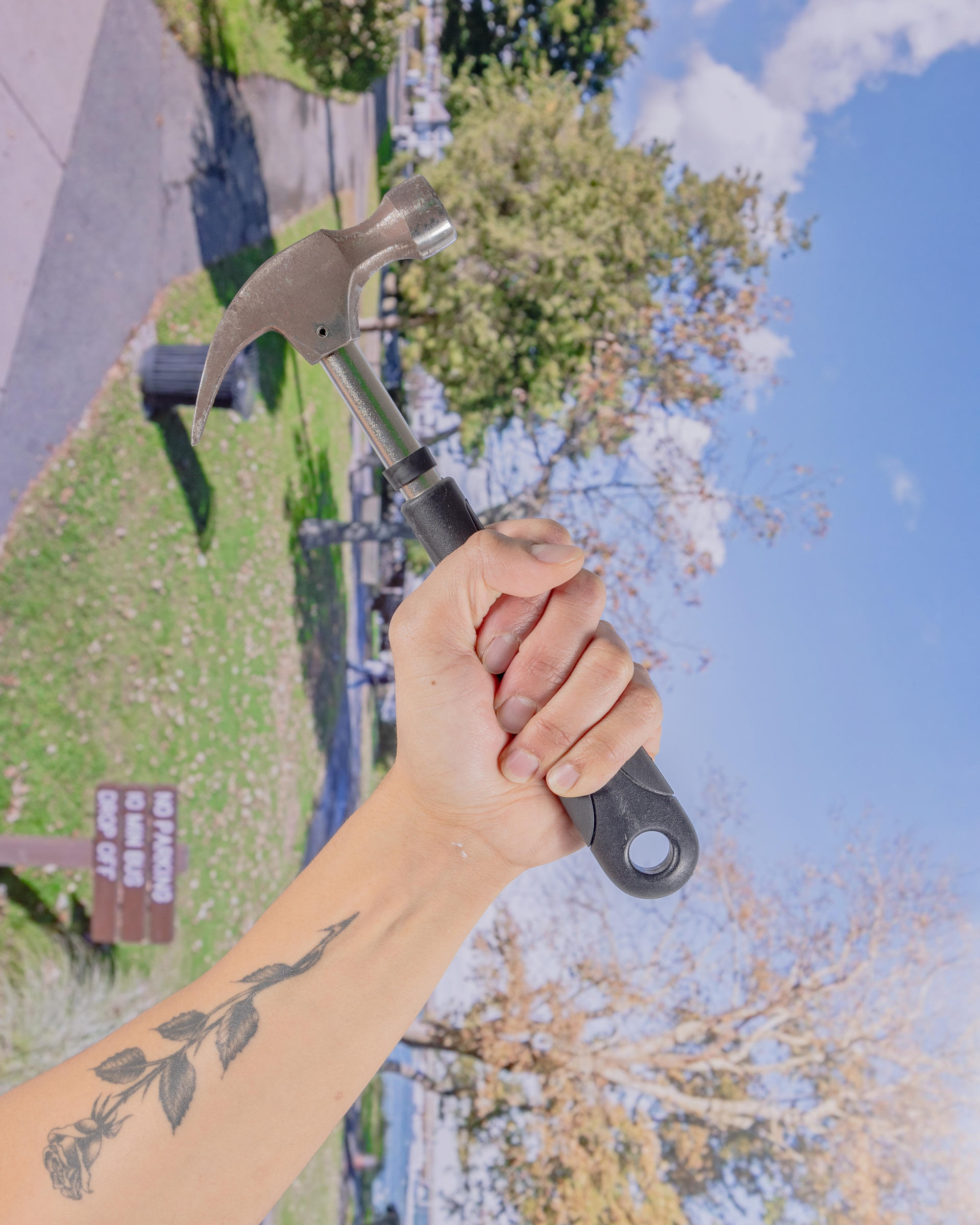 A hand is holding a black and silver hammer, it is against a disoriented backdrop depicting Plymouth, Massachusetts. 