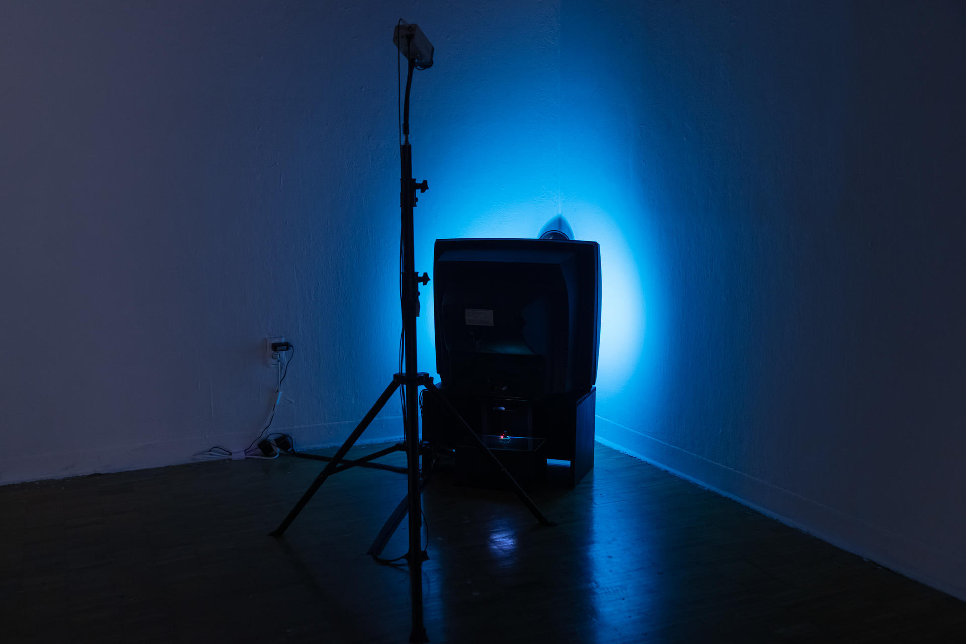 A camera on tripod and a TV placed against a wall corner, reflecting colorful light.