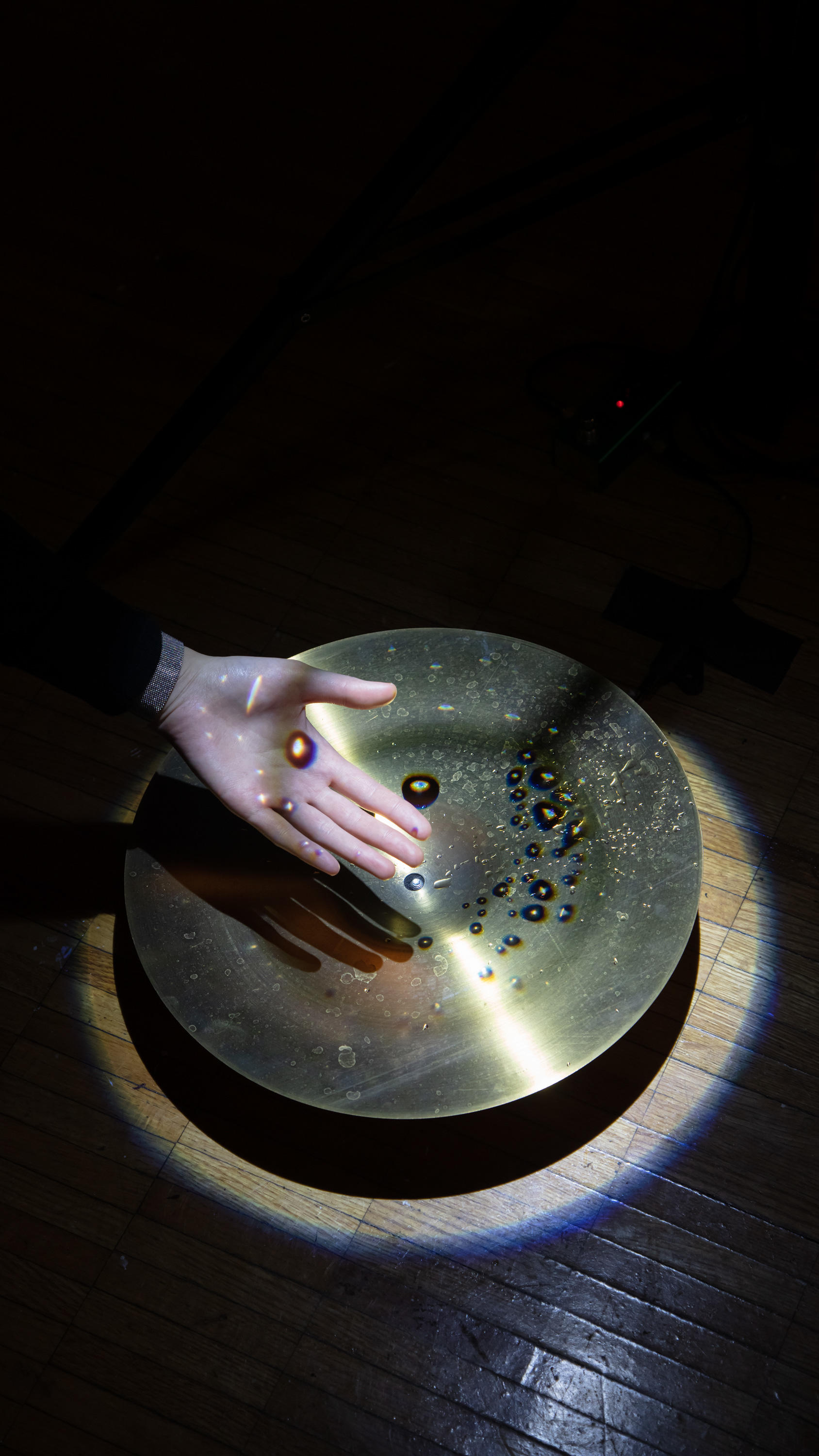 Hand in front of cymbal with water drops projected onto the surface