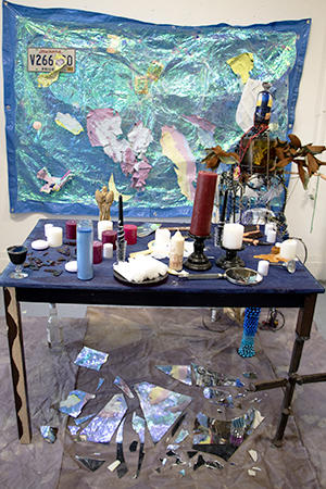 Table with painting and wall piece along with chair sculpture modeled after figure.