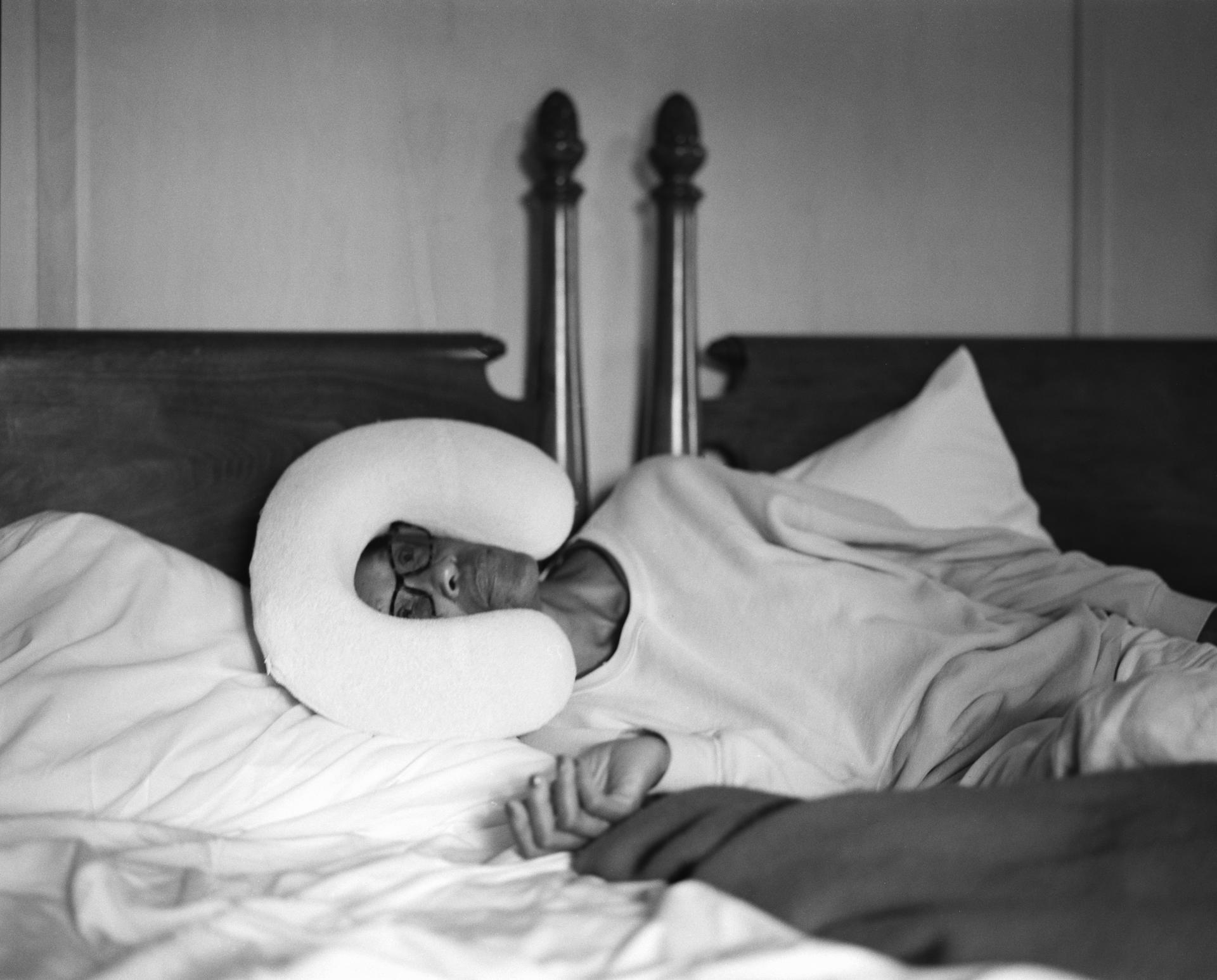 a woman lays on her side on a bed facing the camera, something strange is on her head