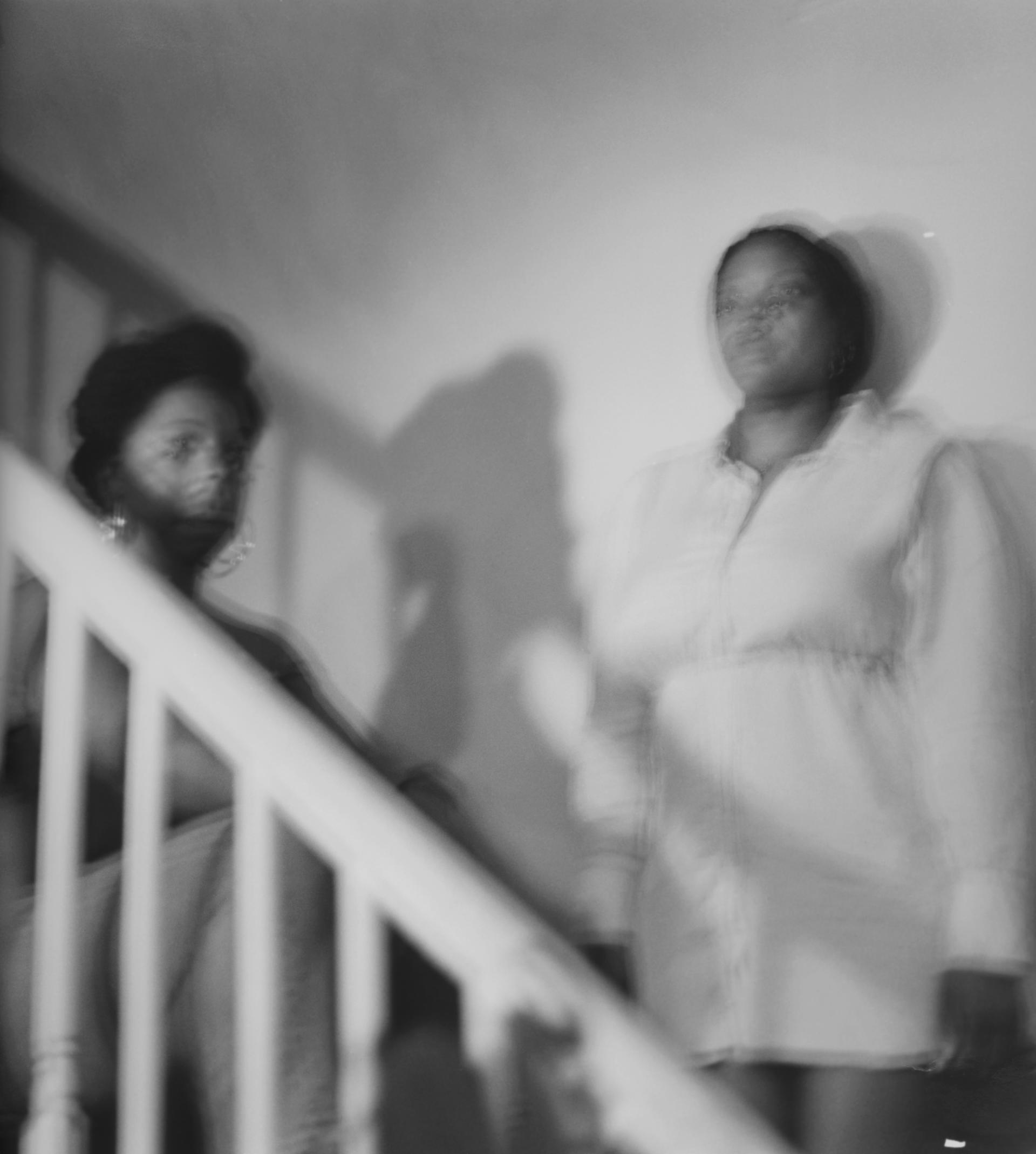 two woman, blurred, stand facing the camera on a staircase