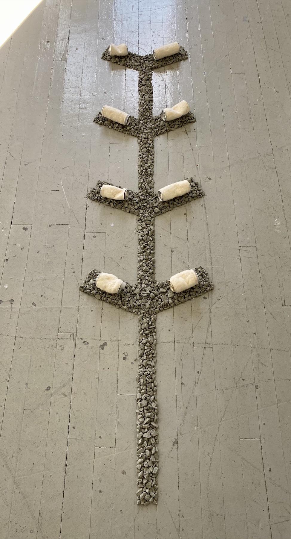 Loose gravel forms a shape on the floor, with felted aluminum cans placed on top. 