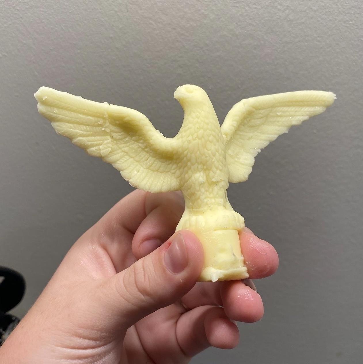 A white person's hand holds a miniature American eagle made of butter. 