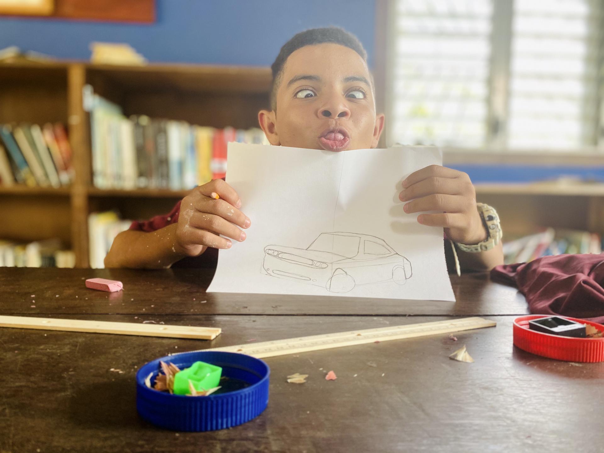 Middle school student holding pencil drawing of a car and making a silly face.