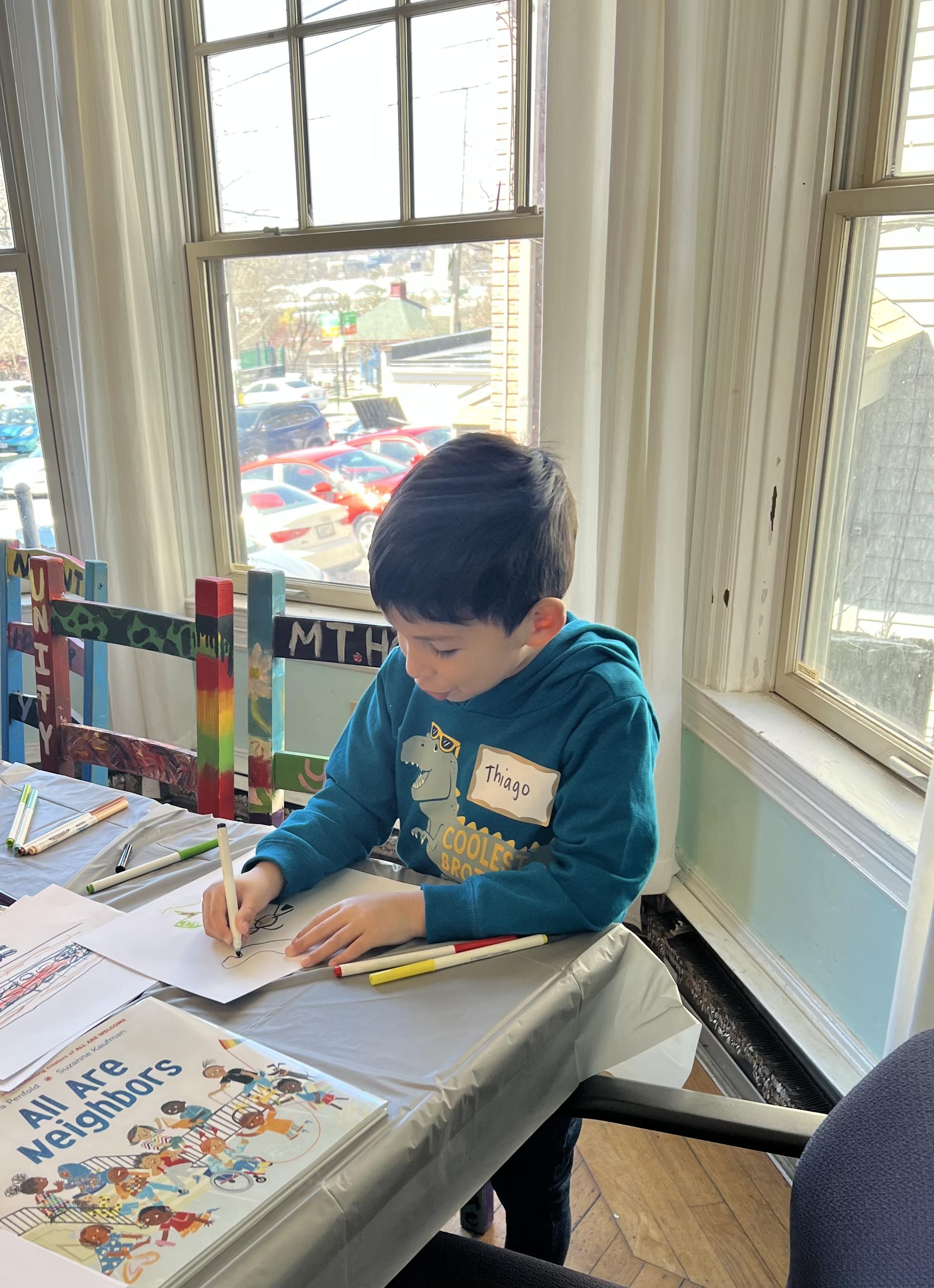 Student sitting at a table and drawing with marker.