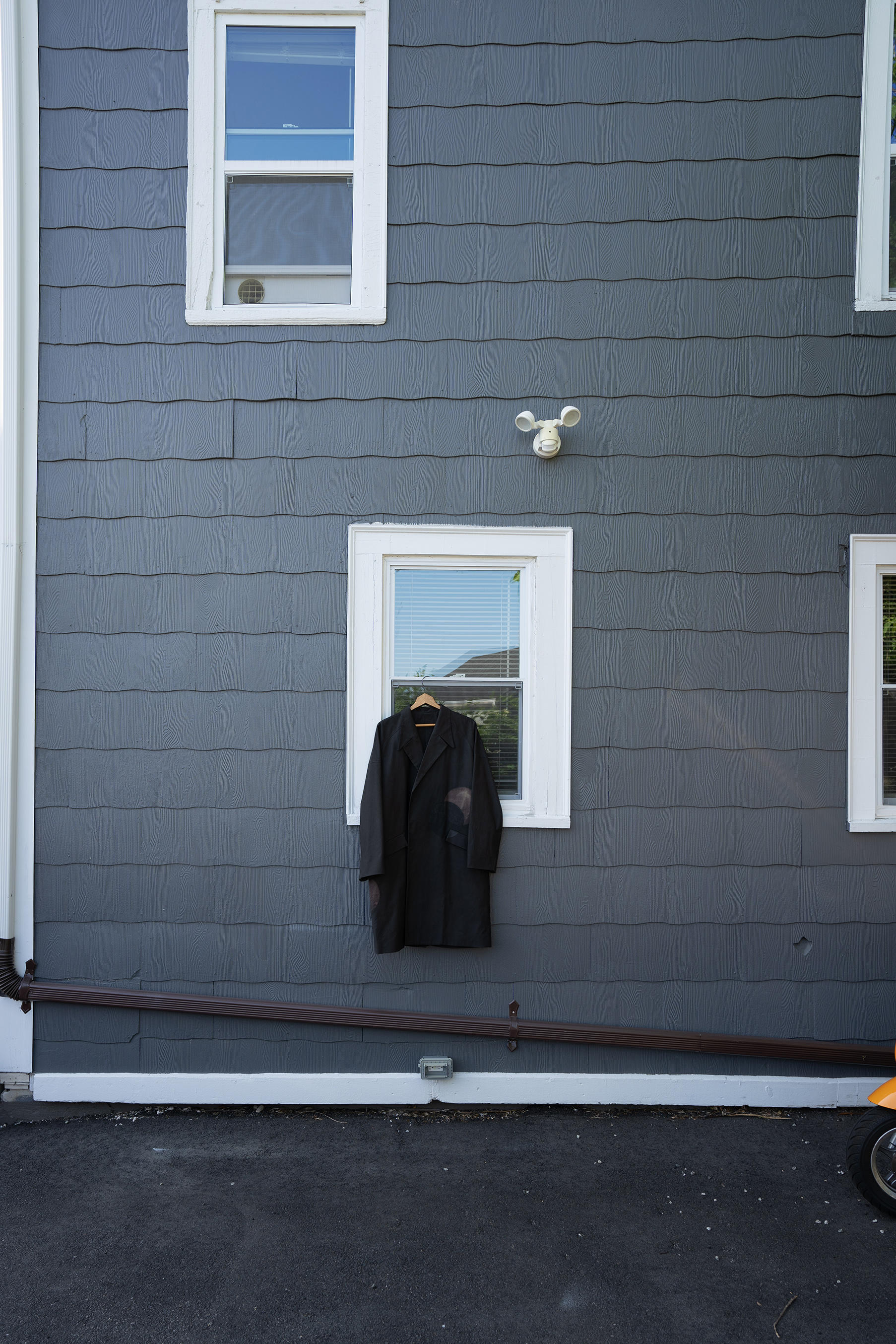 black coat hanging from a window on a grey house