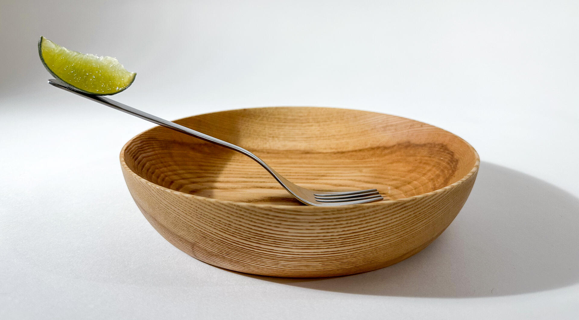 A wooden bowl with a fork magnetically attached to the interior, with a slice of lime balancing on the end of the handle to demonstrate the magnetic pull.