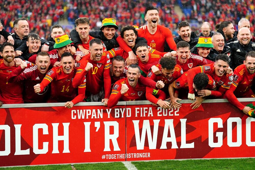 Welsh football players wearing bucket hats and celebrating in front of a banner with the words "thank you to the Red Wall" in Welsh.