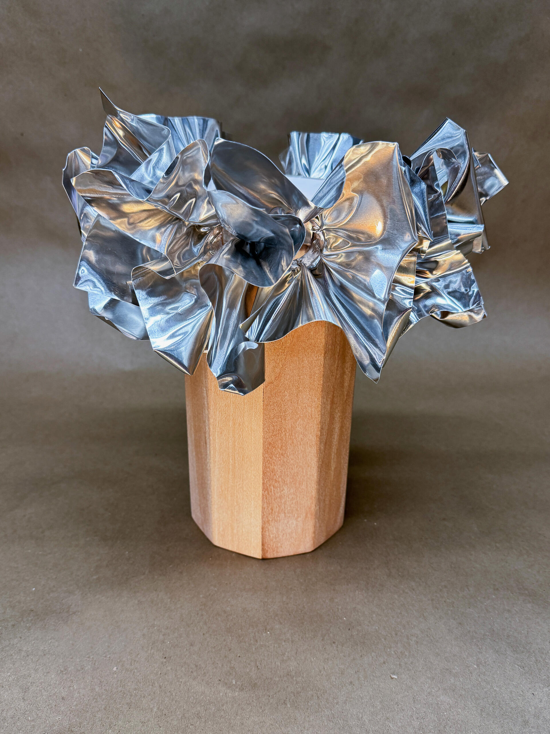A geometric wooden lamp base contrasts with the lampshade, intricately crumpled and shiny aluminum sheets resembling abstract flowers