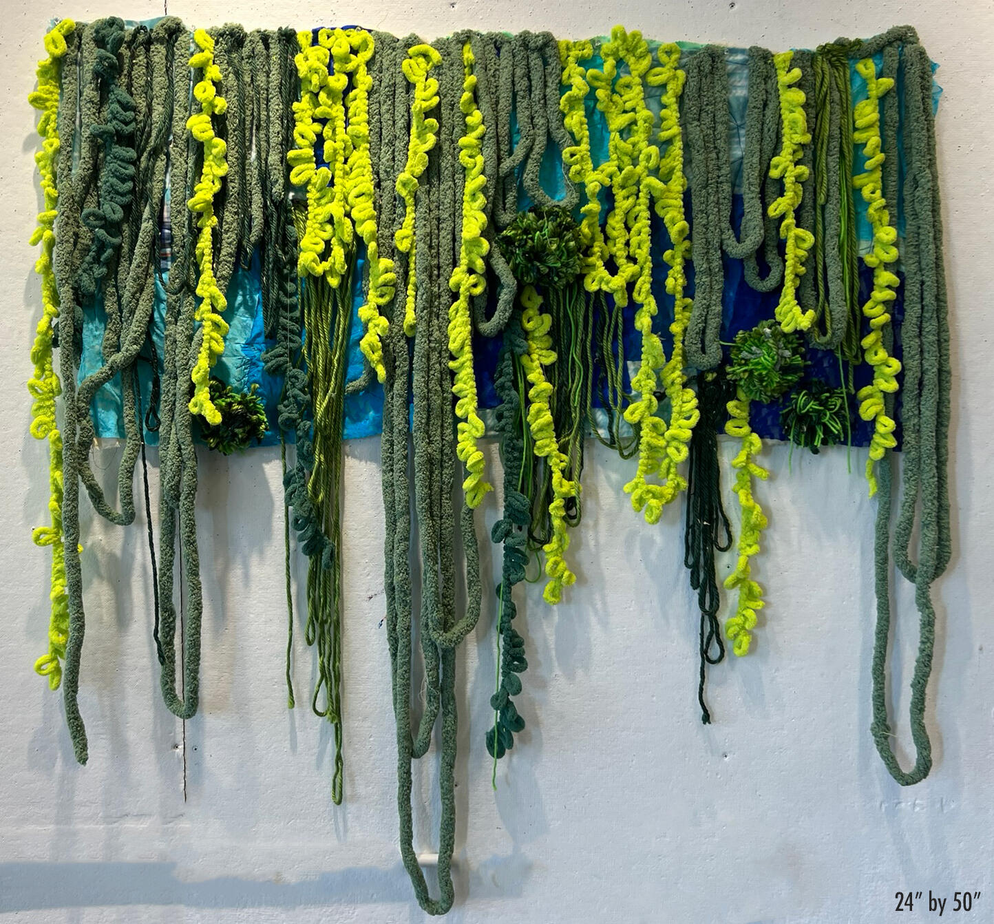 Blue textile rectangular with long thick green yarn strands dangling like vines