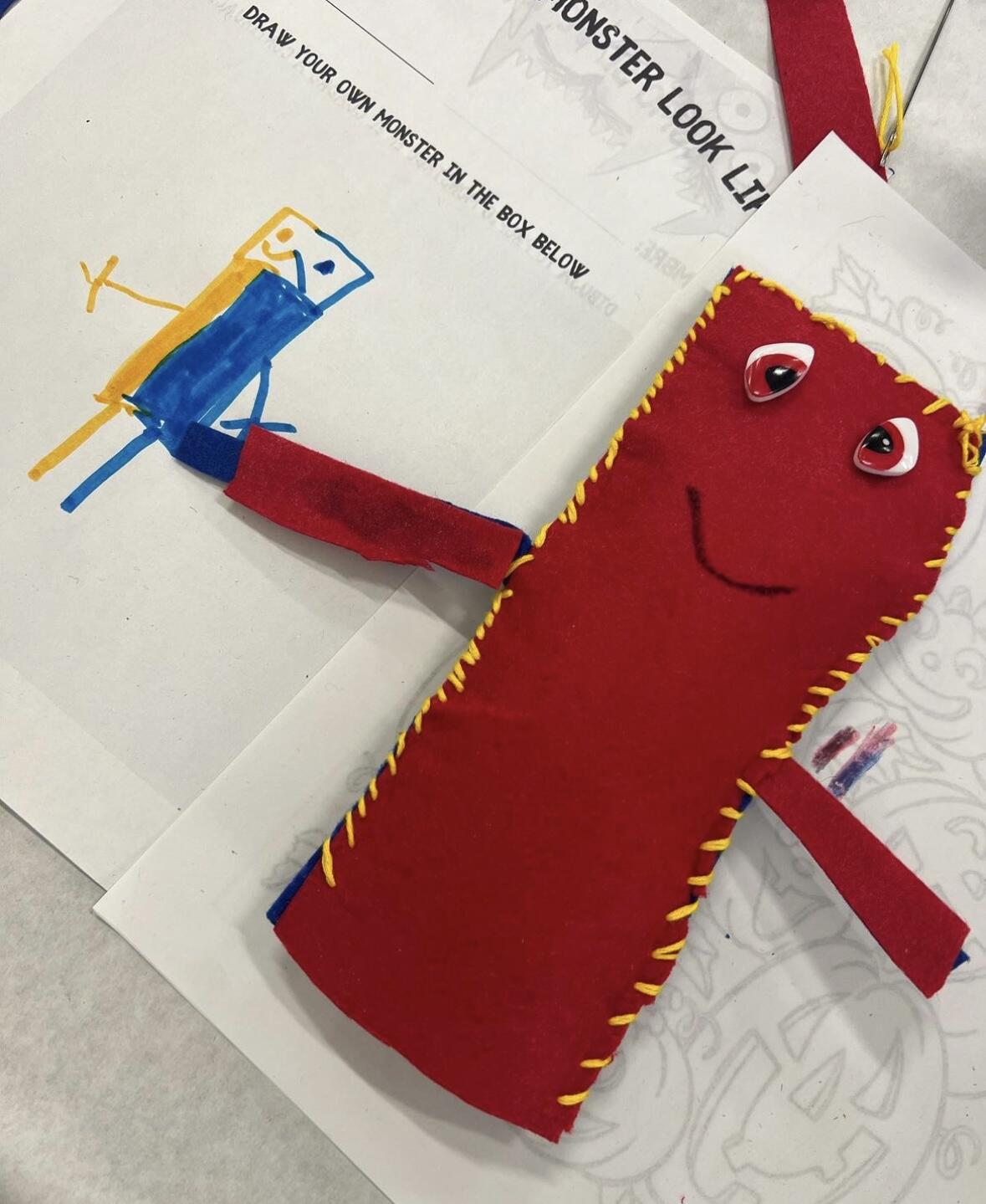 Red hand sewn color monster with red eye and yellow stitching around the rectangular body