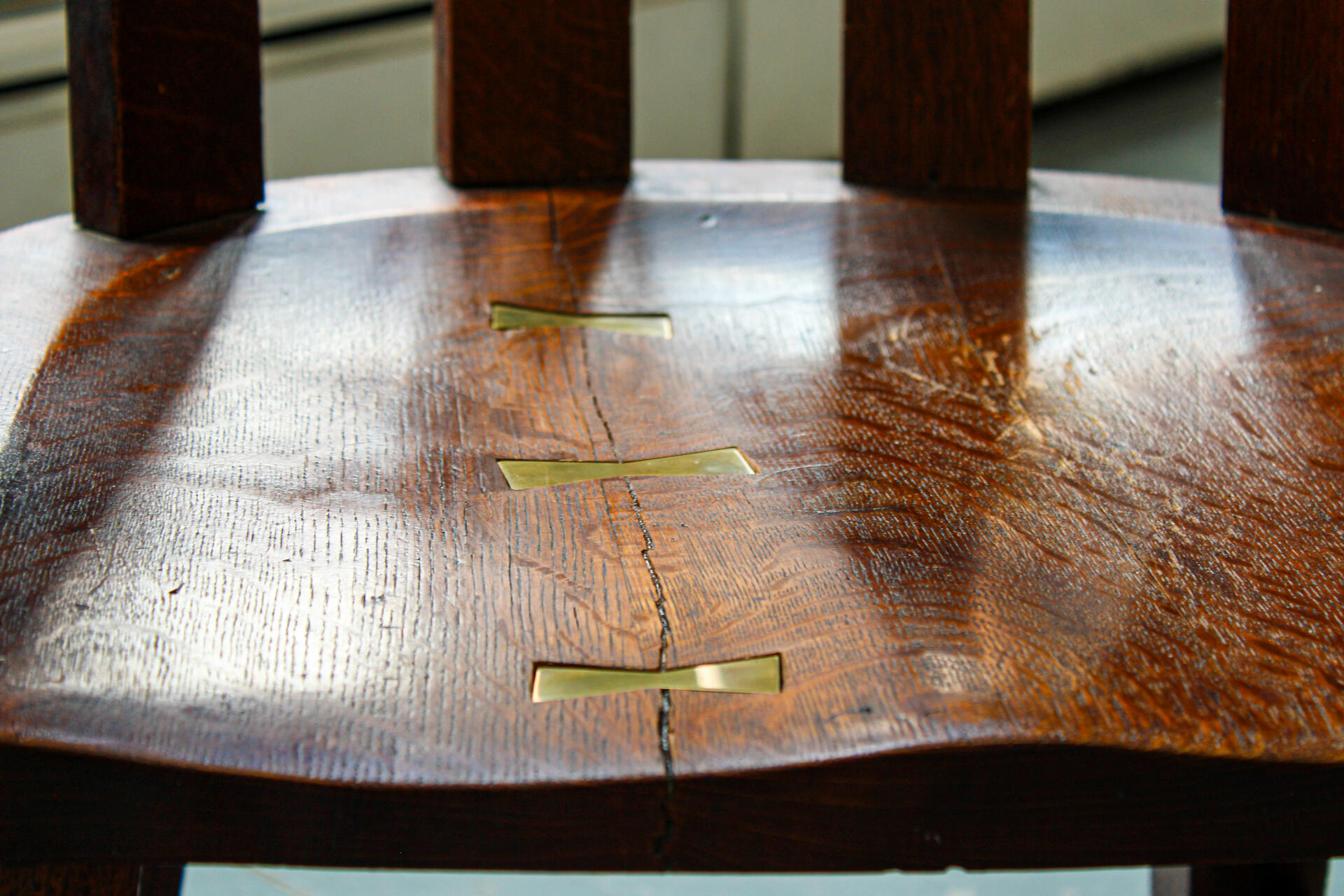 A close up shot of the repaired oak chair highlighting the brass bowties holding together the formerly cracked seat of the chair.