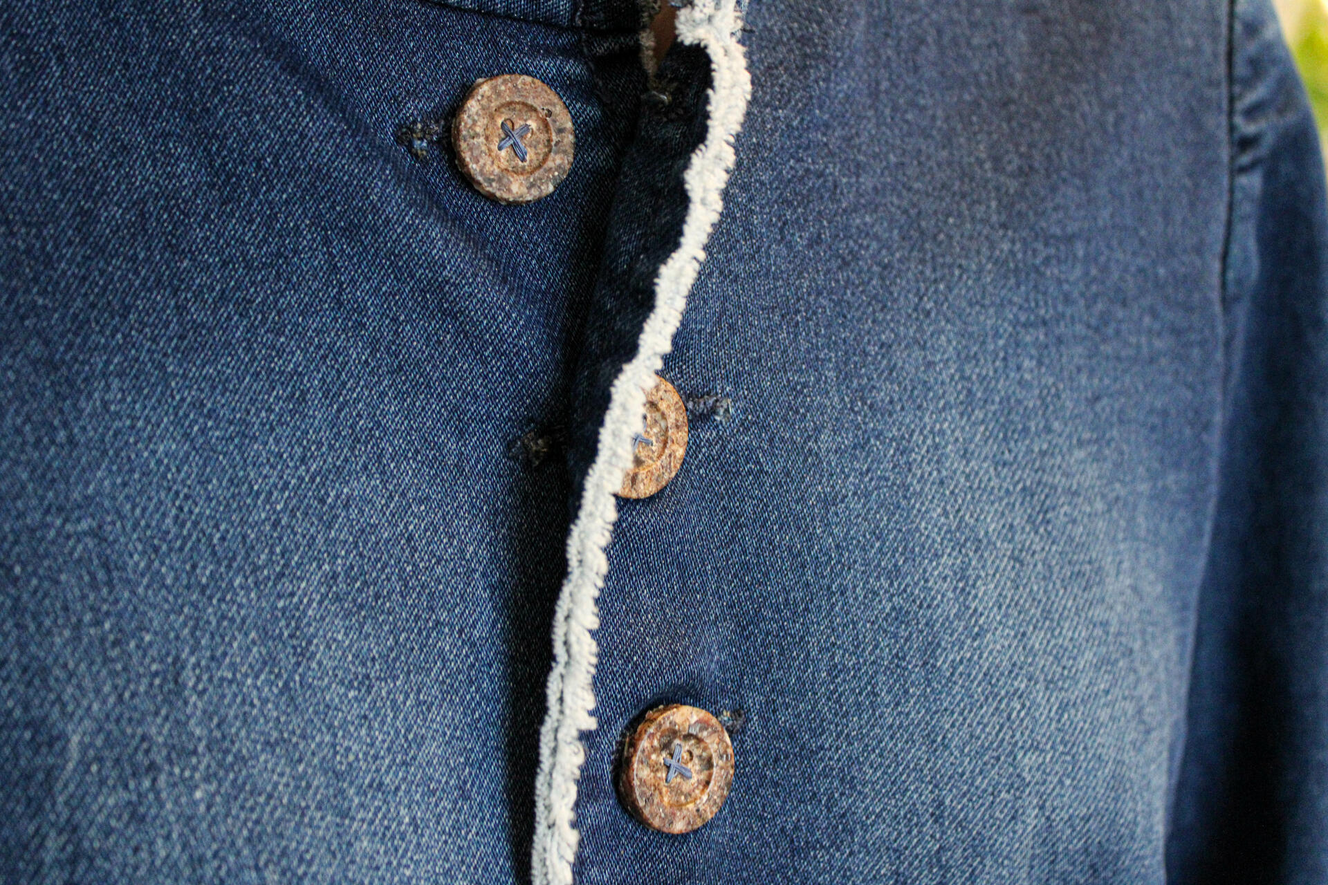 A close-up shot of three buttons made of periwinkle shells ground up and casted back together into the shape of a traditional button. They are stitched with blue thread onto a denim jacket.