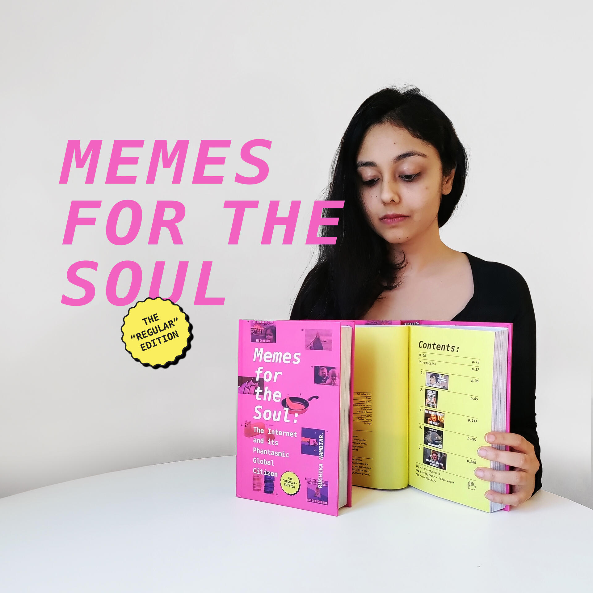 Ruchika Nambiar seated at a table with two copies of a hardcover book propped up in front of her. She is holding one of the books open to display its interior pages.