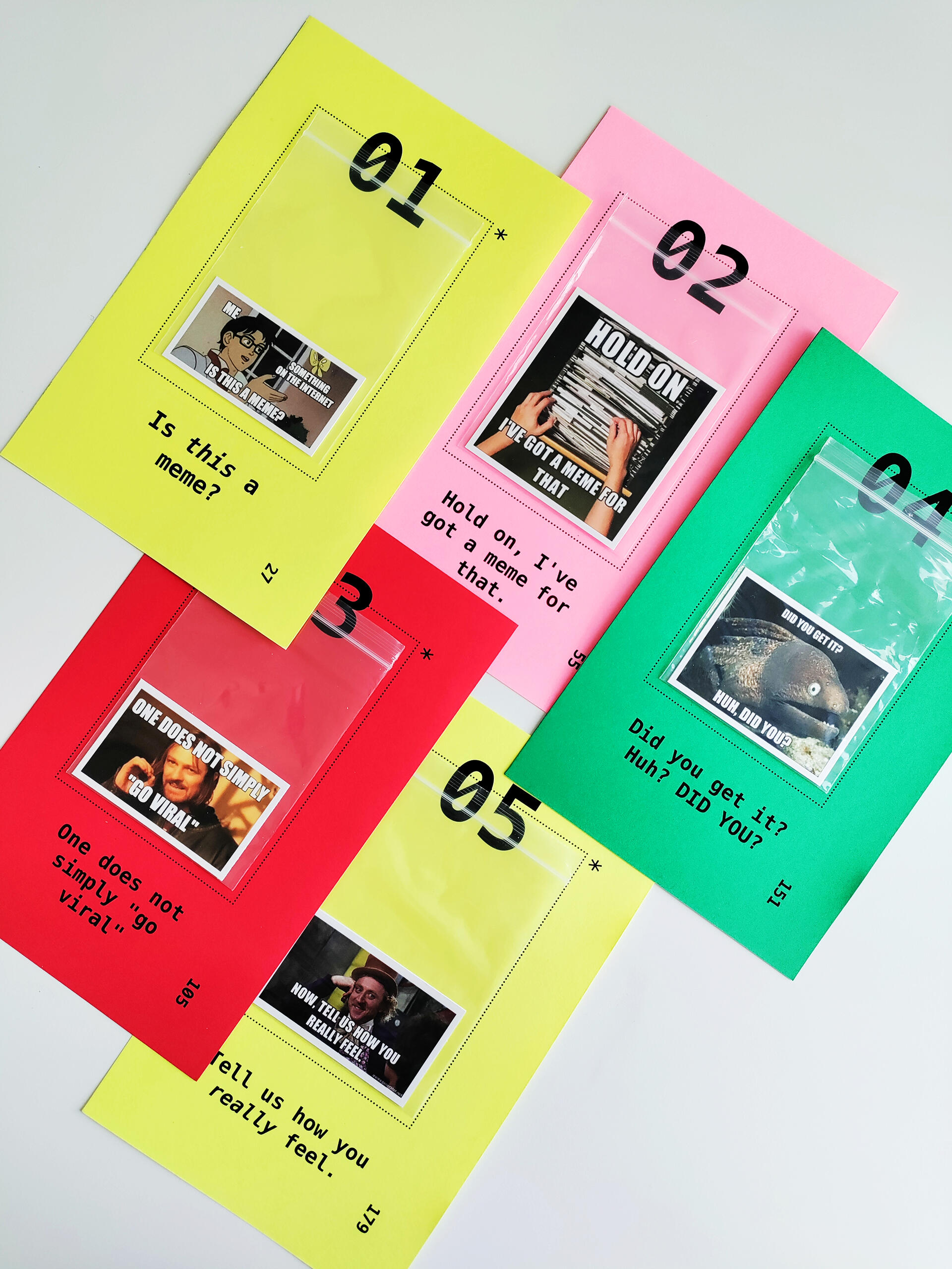 Five colorful loose pages printed with chapter numbers and titles. Each page has a ziploc bag attached to it, inside which is a printout of an internet meme. 