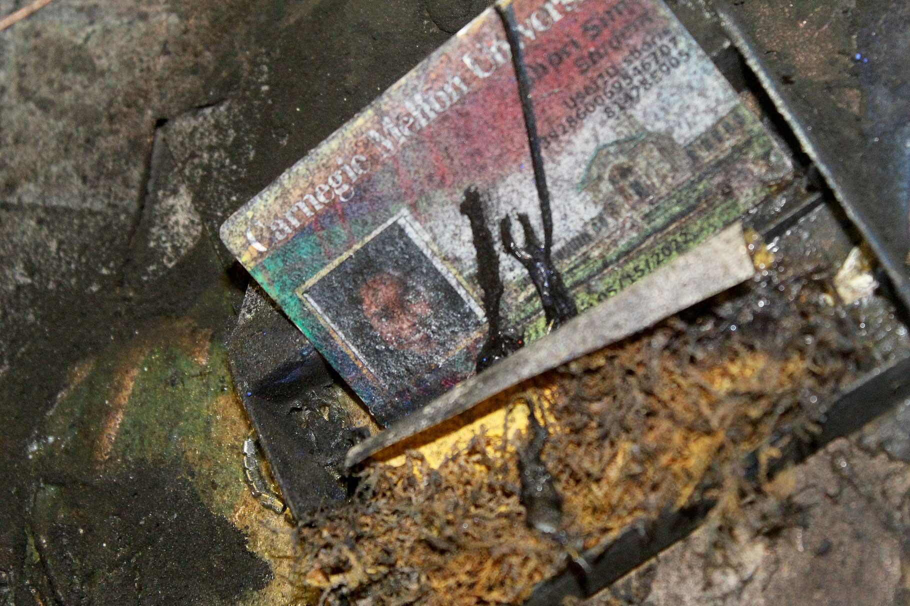 The image shows a close-up of STREETTRASH, featuring the artist's undergraduate student ID covered in thick black liquid and flecks of aerosol paint.