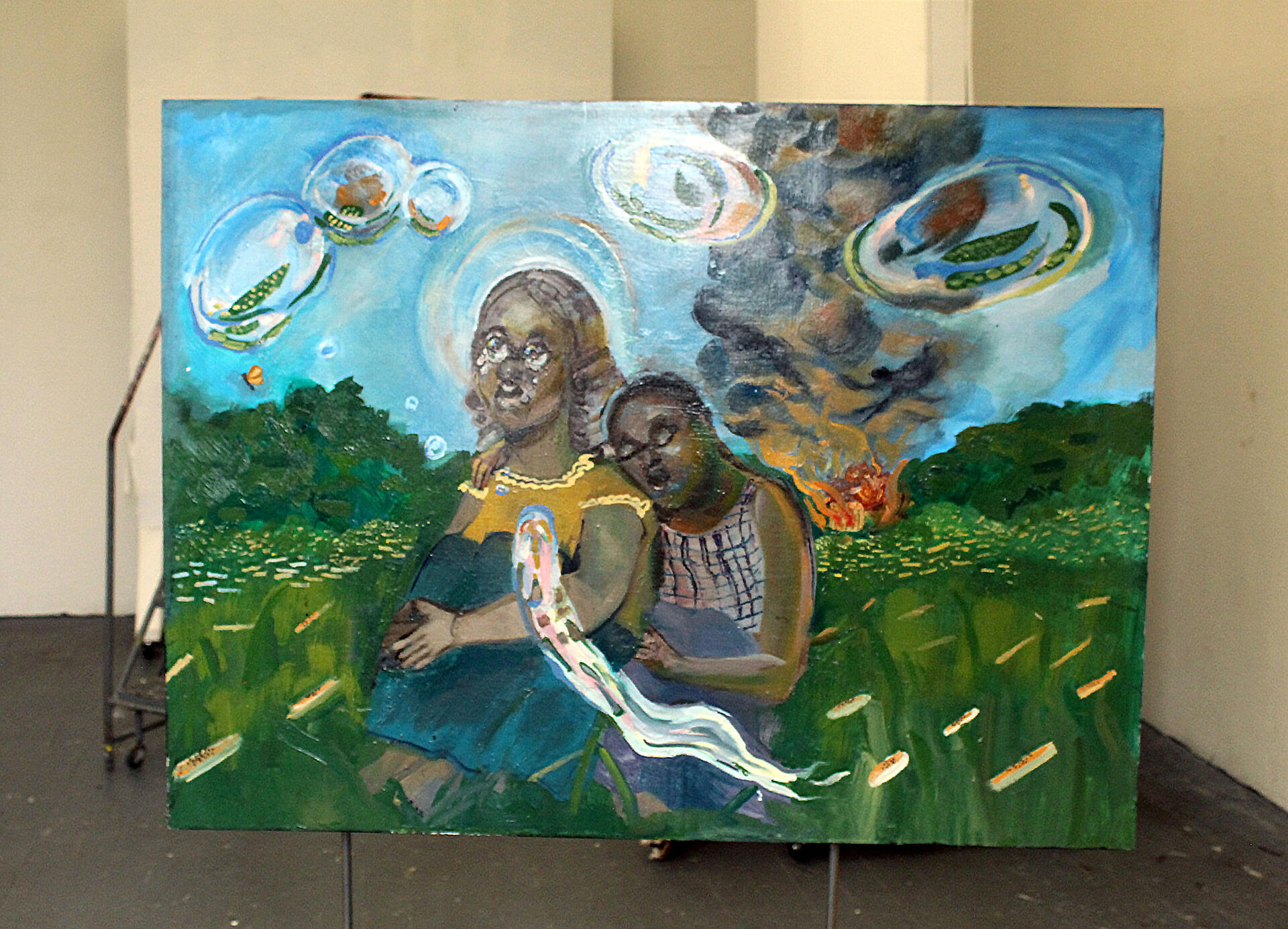 A larger rectangular oil painting on board, supported by a metal structure. The painting depicts two girls sitting in front of a burning house as bubbles float by.