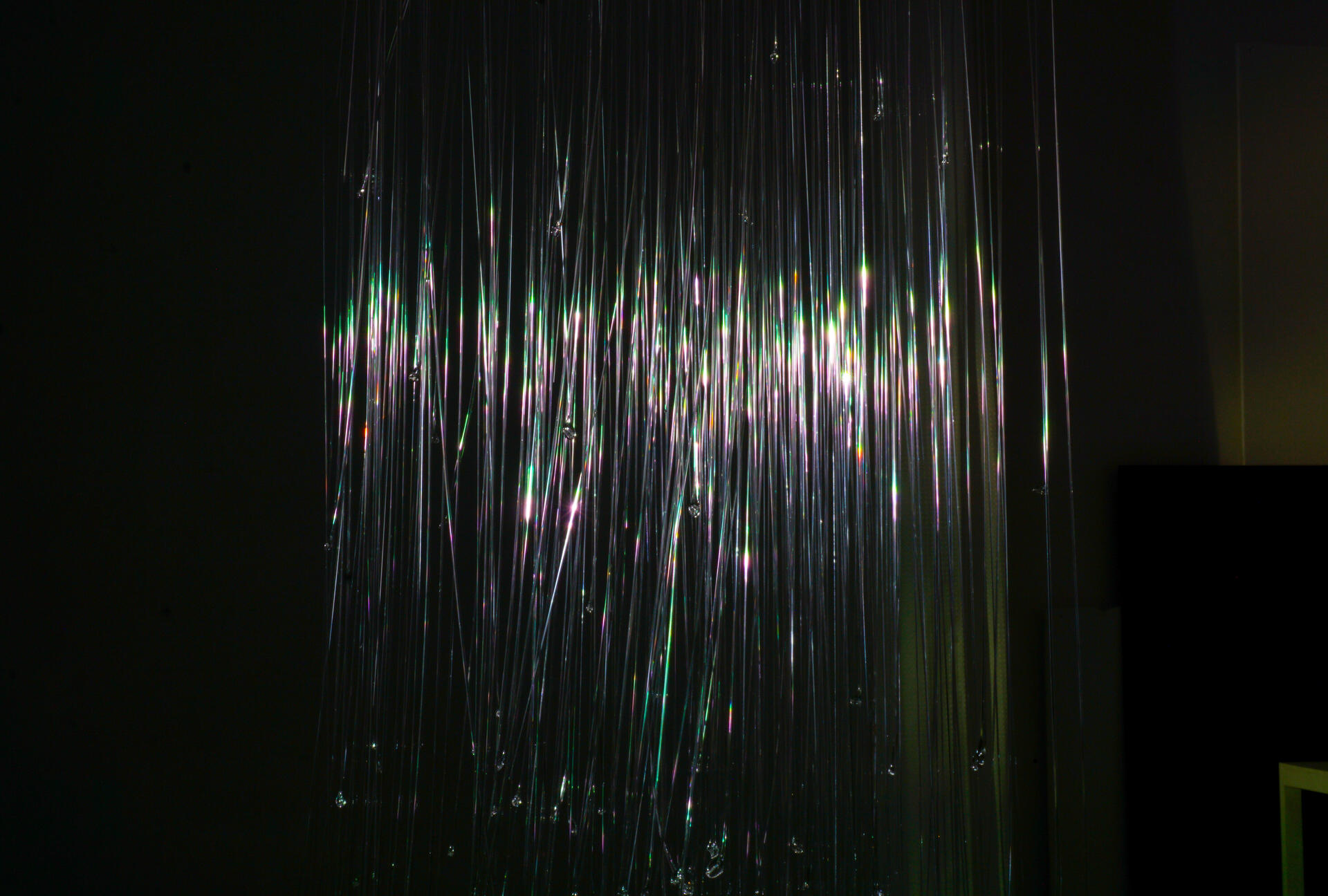 Hundreds of glass fibers suspended in the room, with iridescent light reflected on the surface