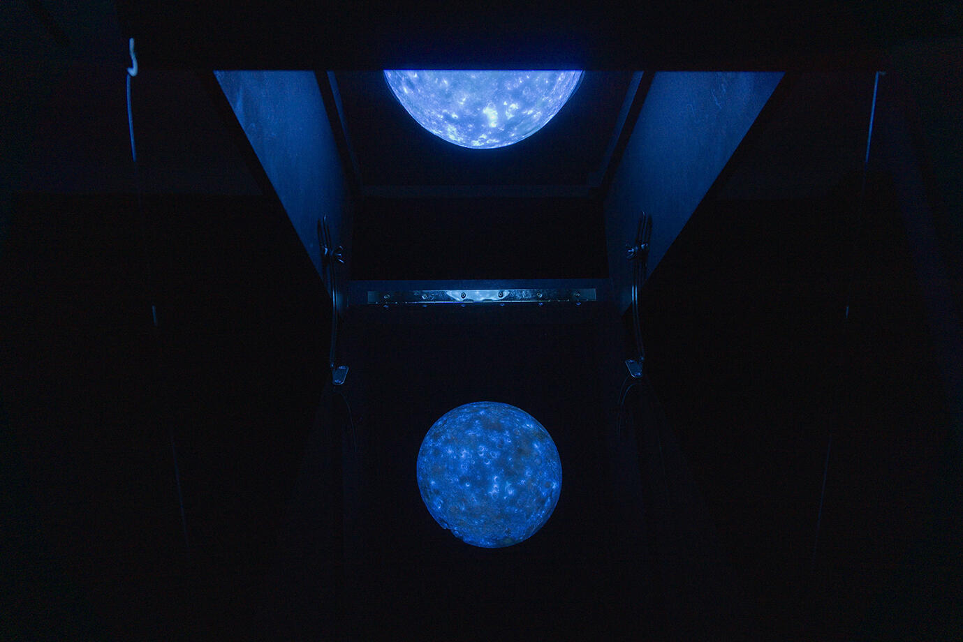 A fluorescent blue moon appears in a dark room, reflecting off an angled acrylic sheet, creating a captivating and ethereal visual effect.