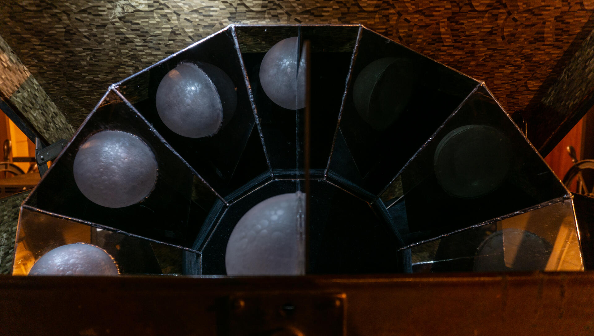 In an antique suitcase, a reflective device composed of multiple mirror structures is placed to showcase the various phases of the moon through a semi-circular glass moon at the center.